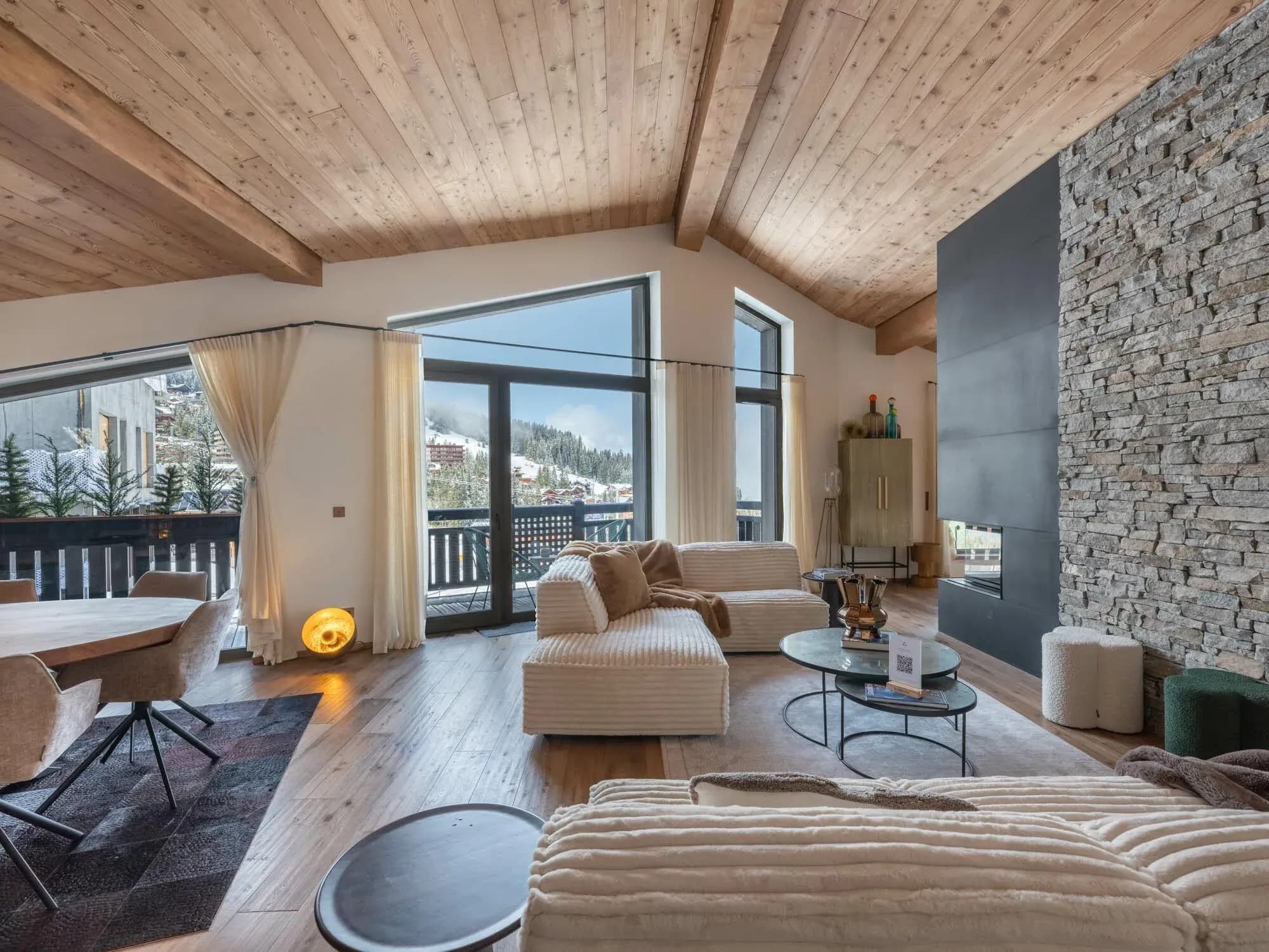 Living room with cream sofas, stone wall fireplace and balcony doors facing the slopes