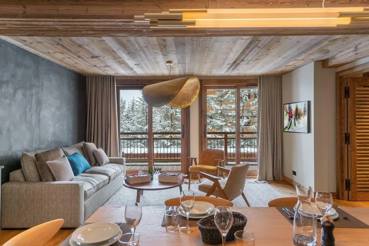 Lounge with grey sofa, two armchairs and balcony doors onto snowy pines