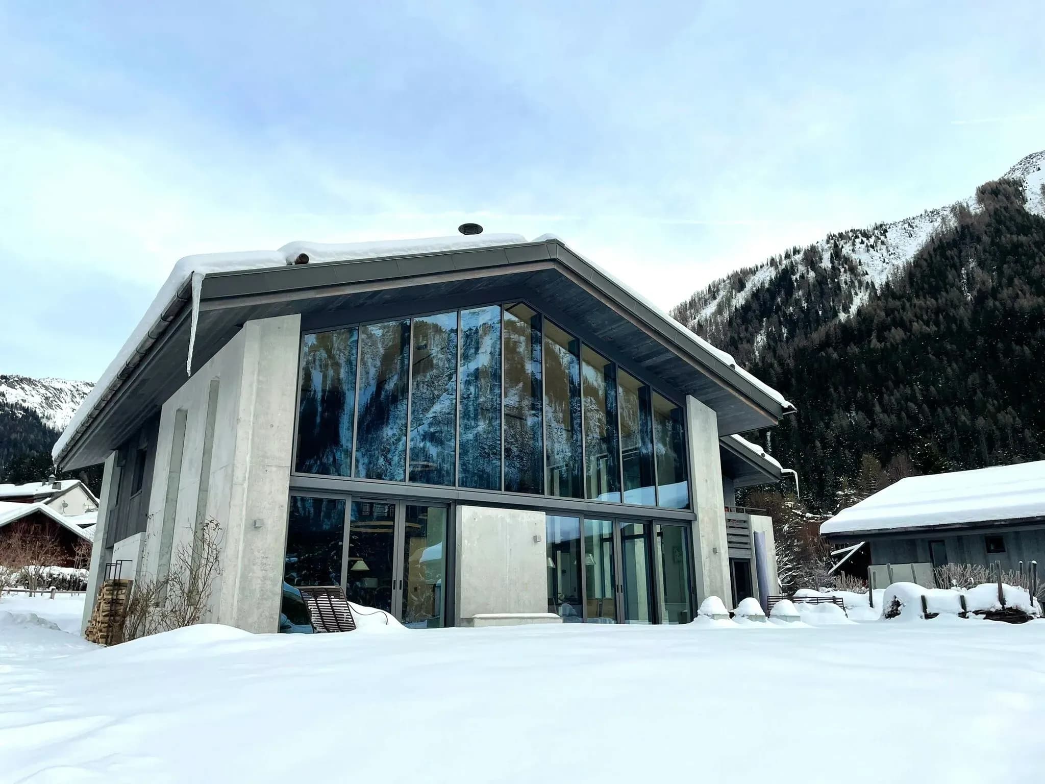 Modern alpine chalet with floor-to-ceiling windows; mountain valley views