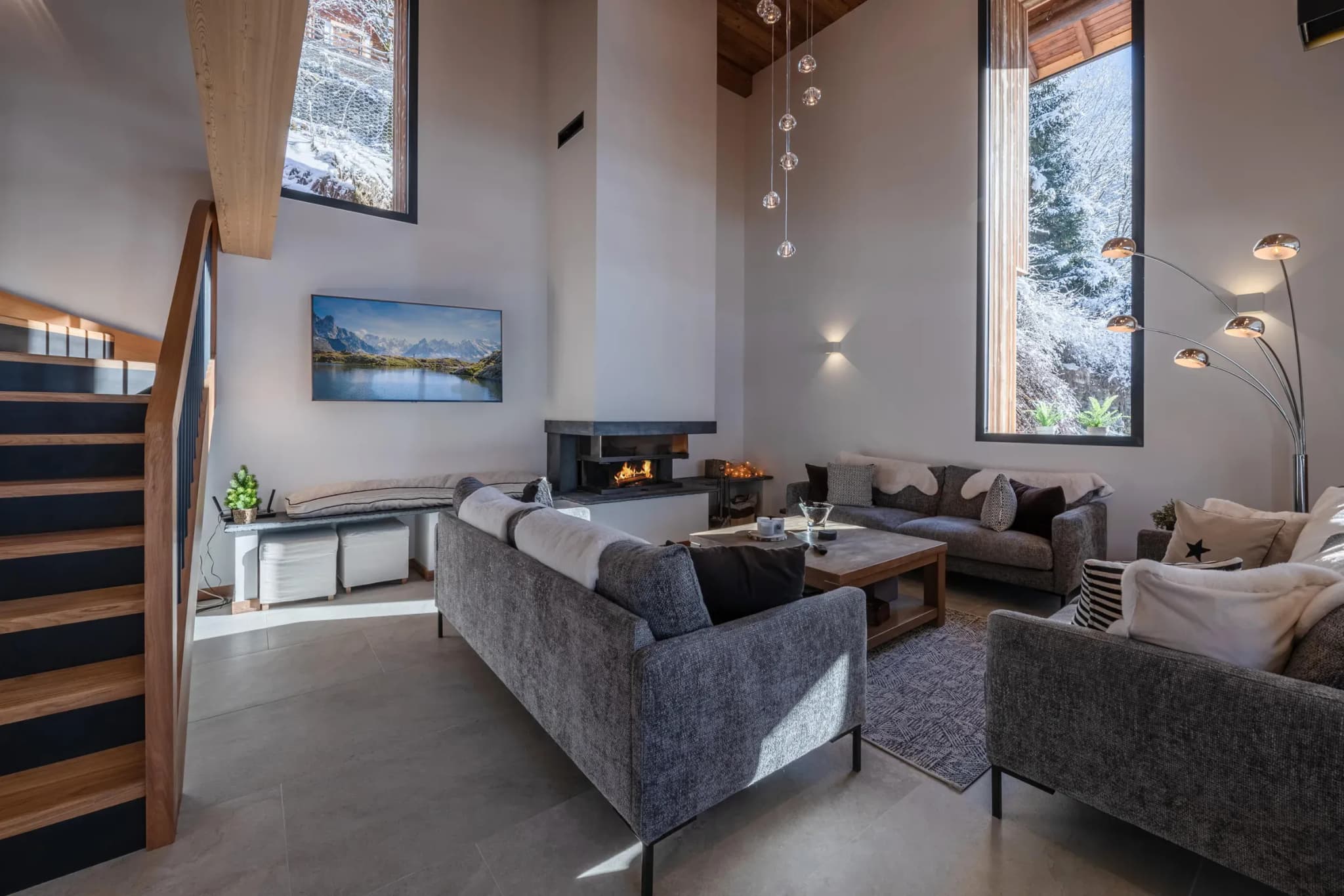 Double-height living room with corner fireplace, two grey sofas and tall windows