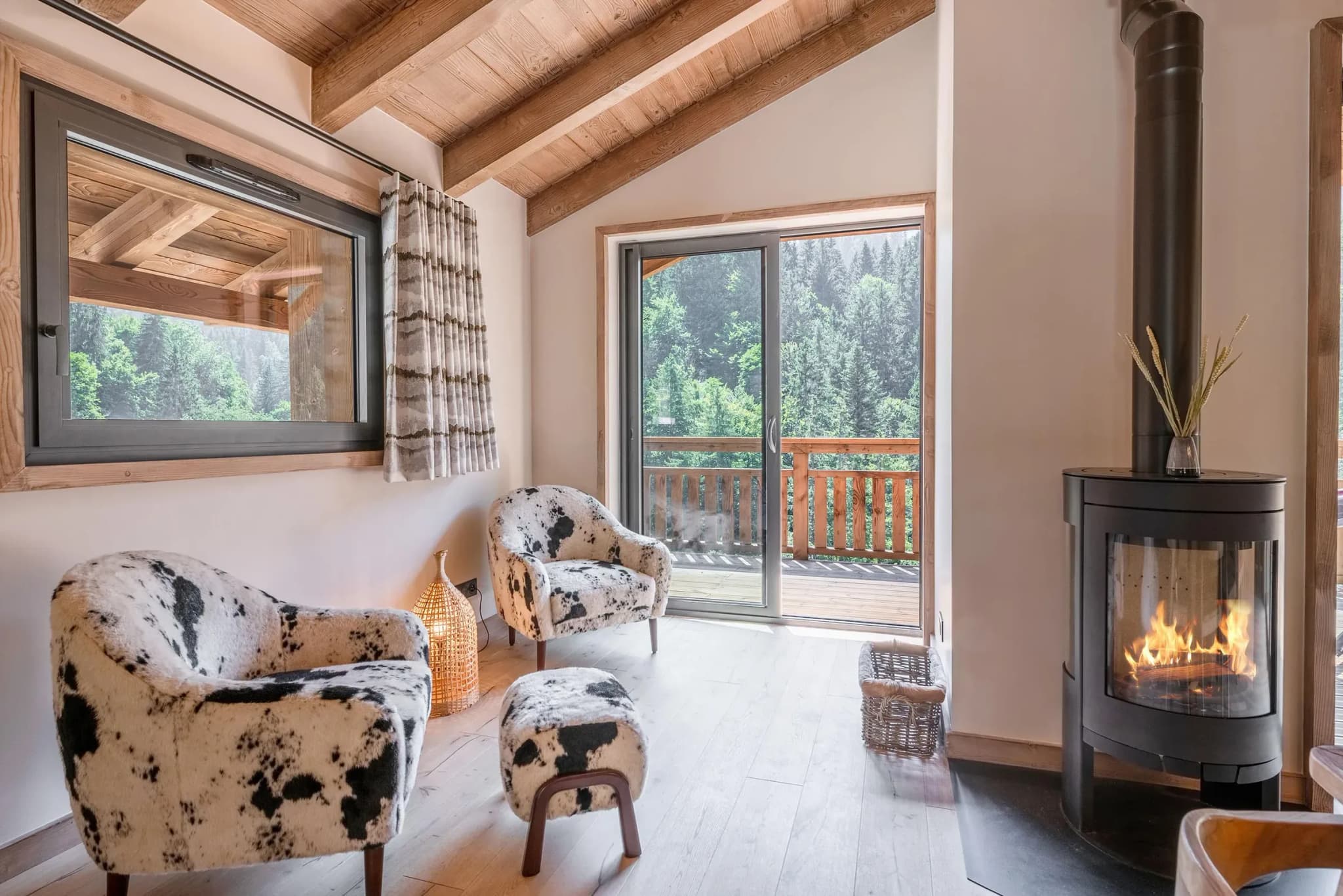 Lounge corner with cowhide-print armchairs, wood stove and balcony door to forest view