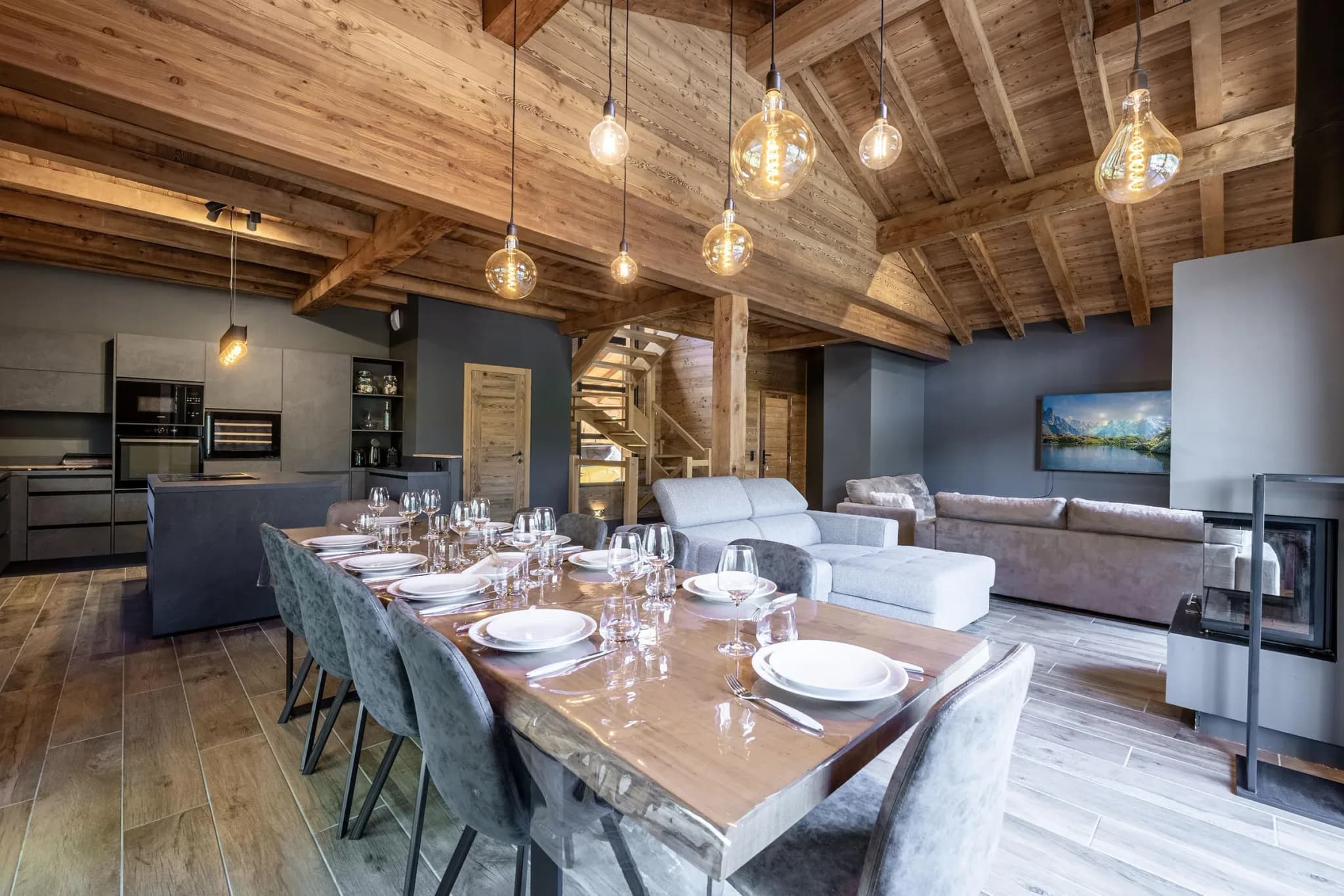 Dining table with eight grey chairs, open kitchen and fireplace behind