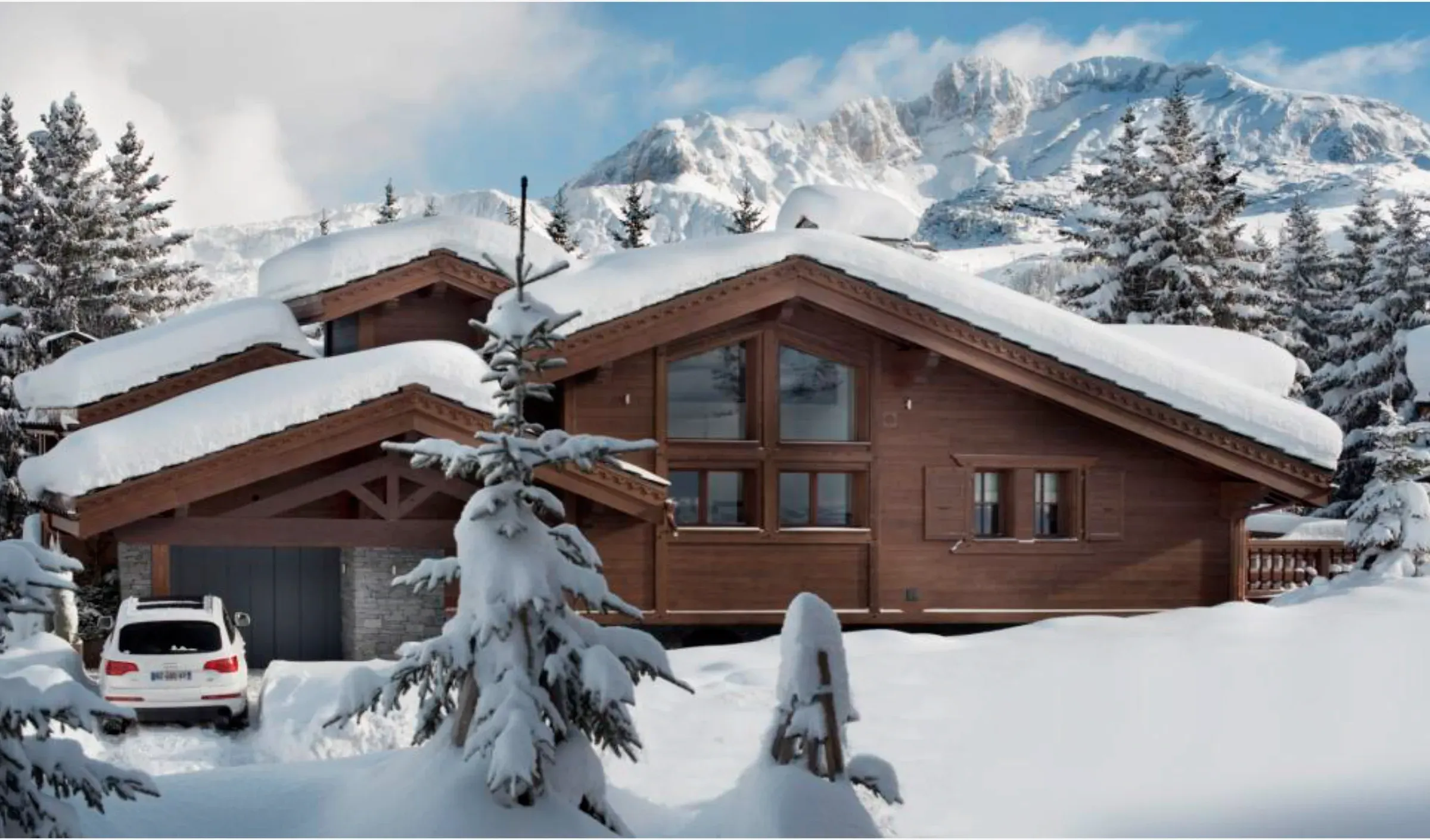 Timber chalet with snow-covered roofs, garage and mountain backdrop