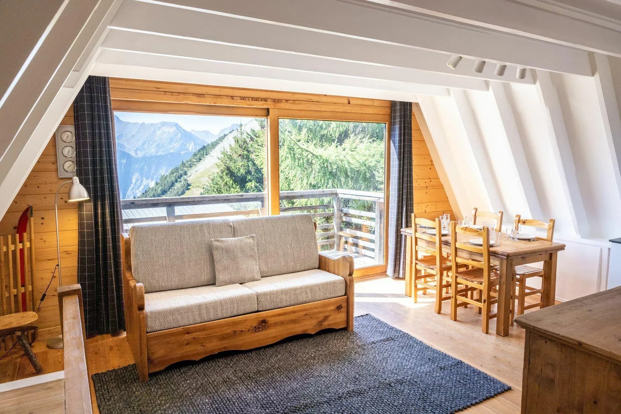 Living area with sofa bed, dining table and balcony view of the mountains