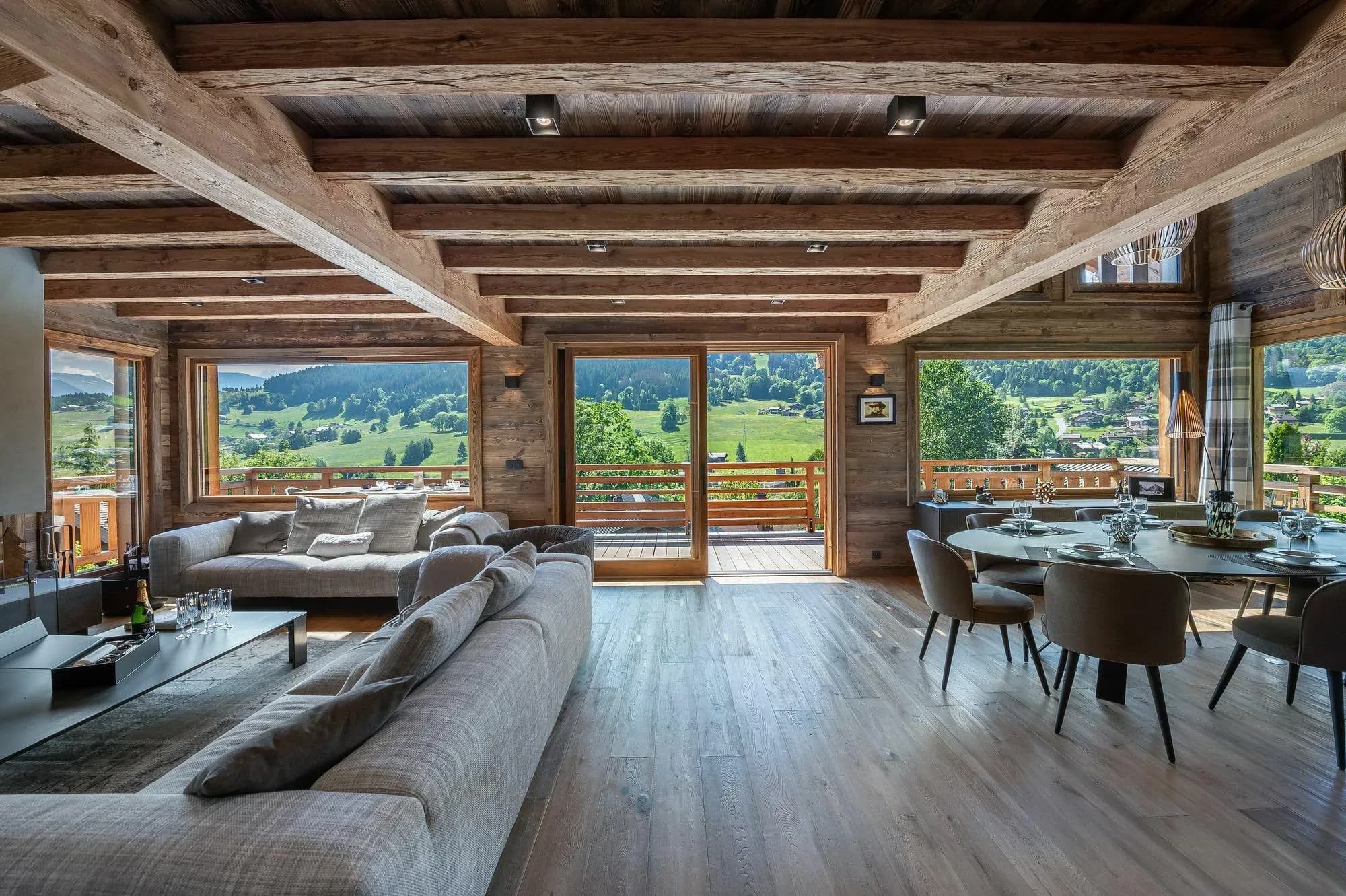 Open living and dining area with exposed beams; valley views from multiple French doors