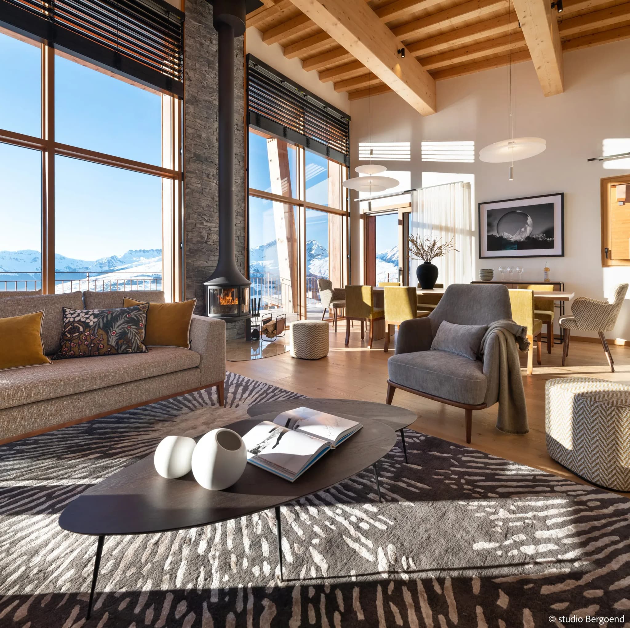 Living room with hanging wood fireplace, sofa, armchairs and mountain views through floor-to-ceiling windows