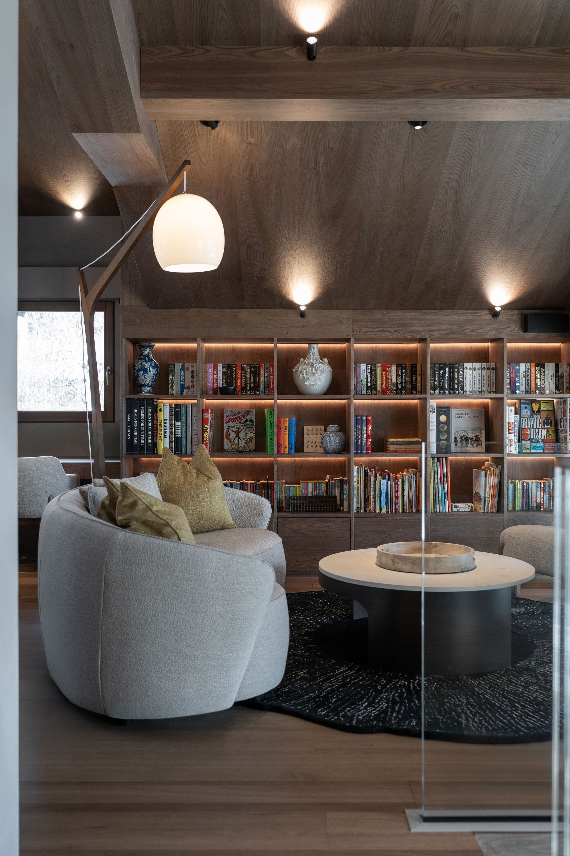 Library lounge with curved seating, floor-to-ceiling shelving, and pendant lighting