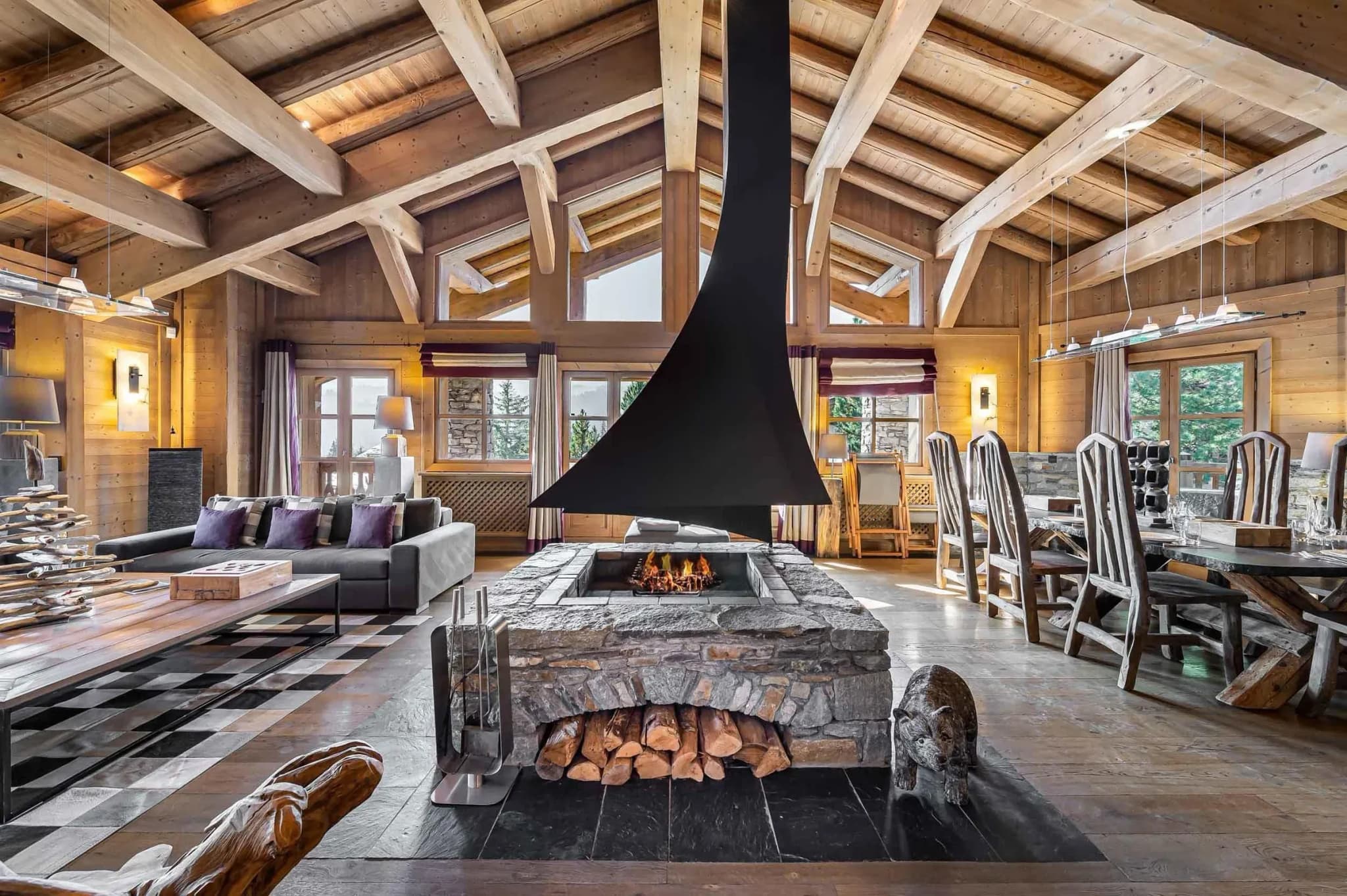 Open living and dining area with central suspended fireplace and stone hearth