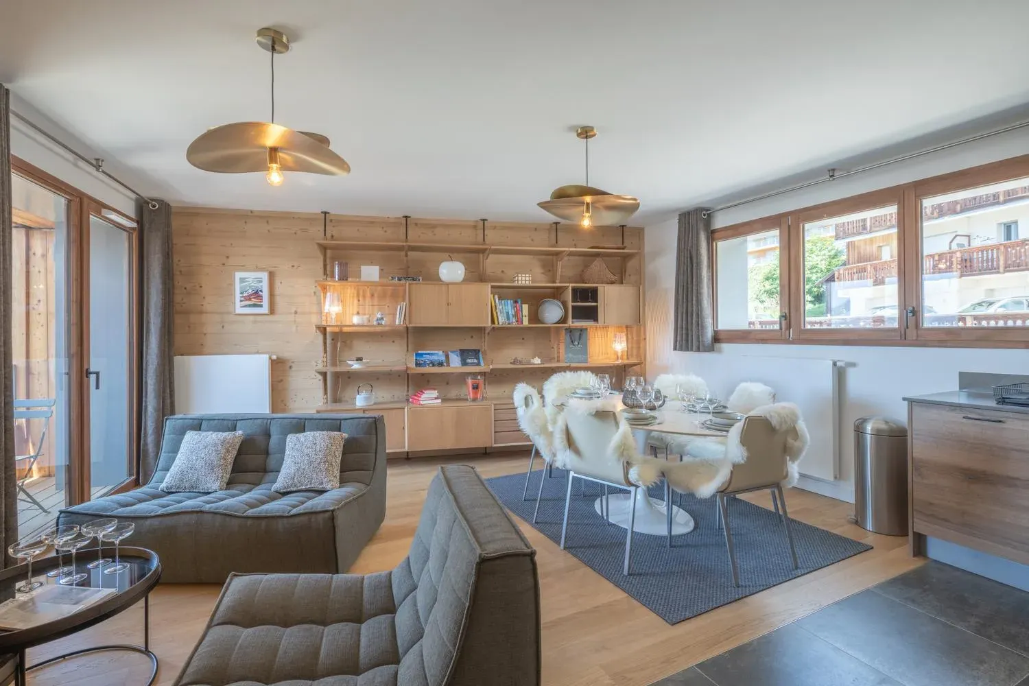 Open-plan lounge with two grey sofas, dining table and wooden shelving