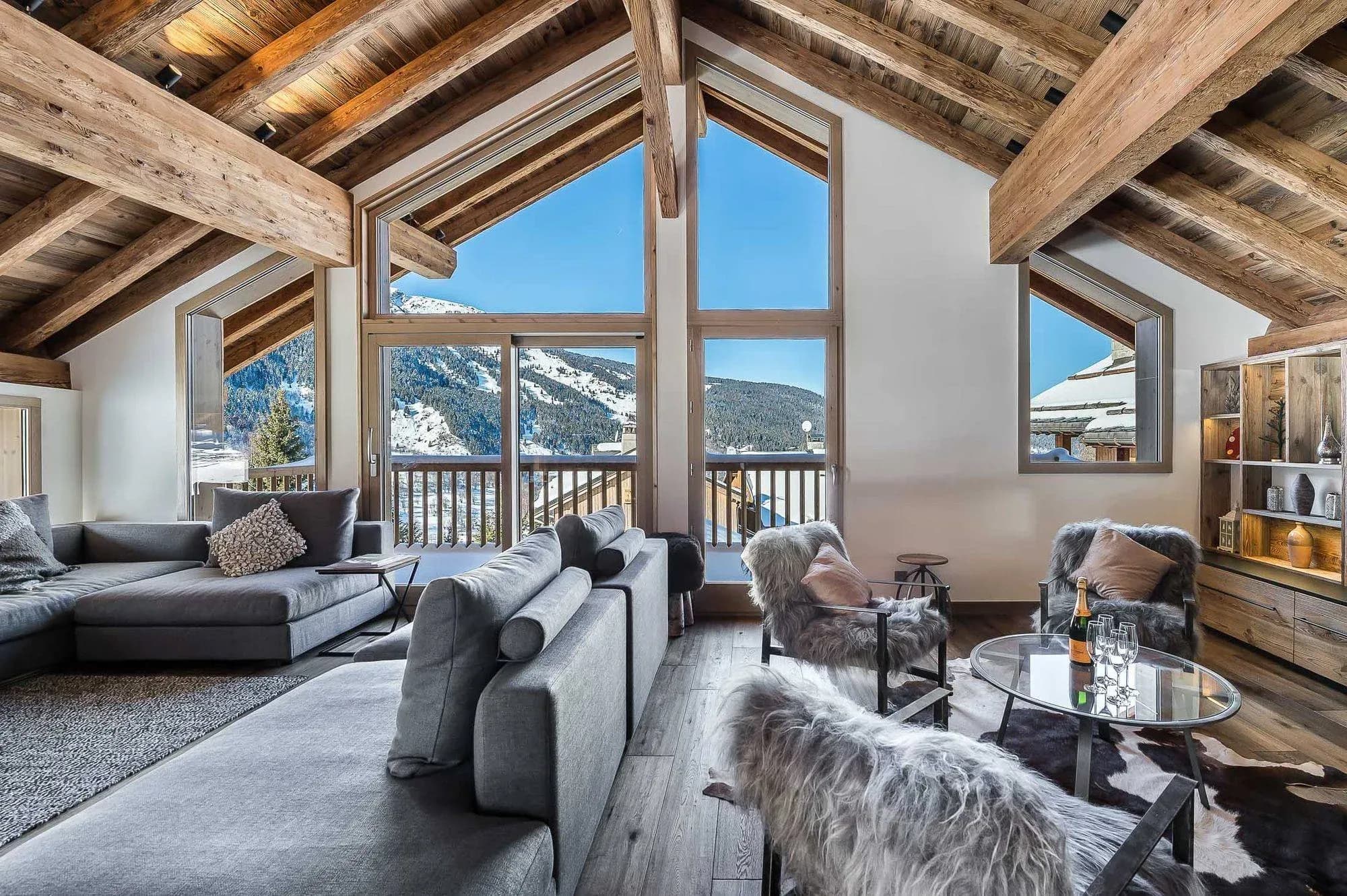 Living room with grey sofas, fur armchairs and mountain views through tall windows