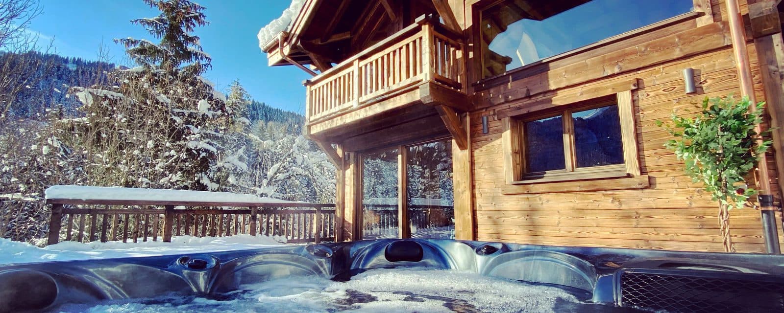 Outdoor hot tub beside the timber chalet and snow-covered deck