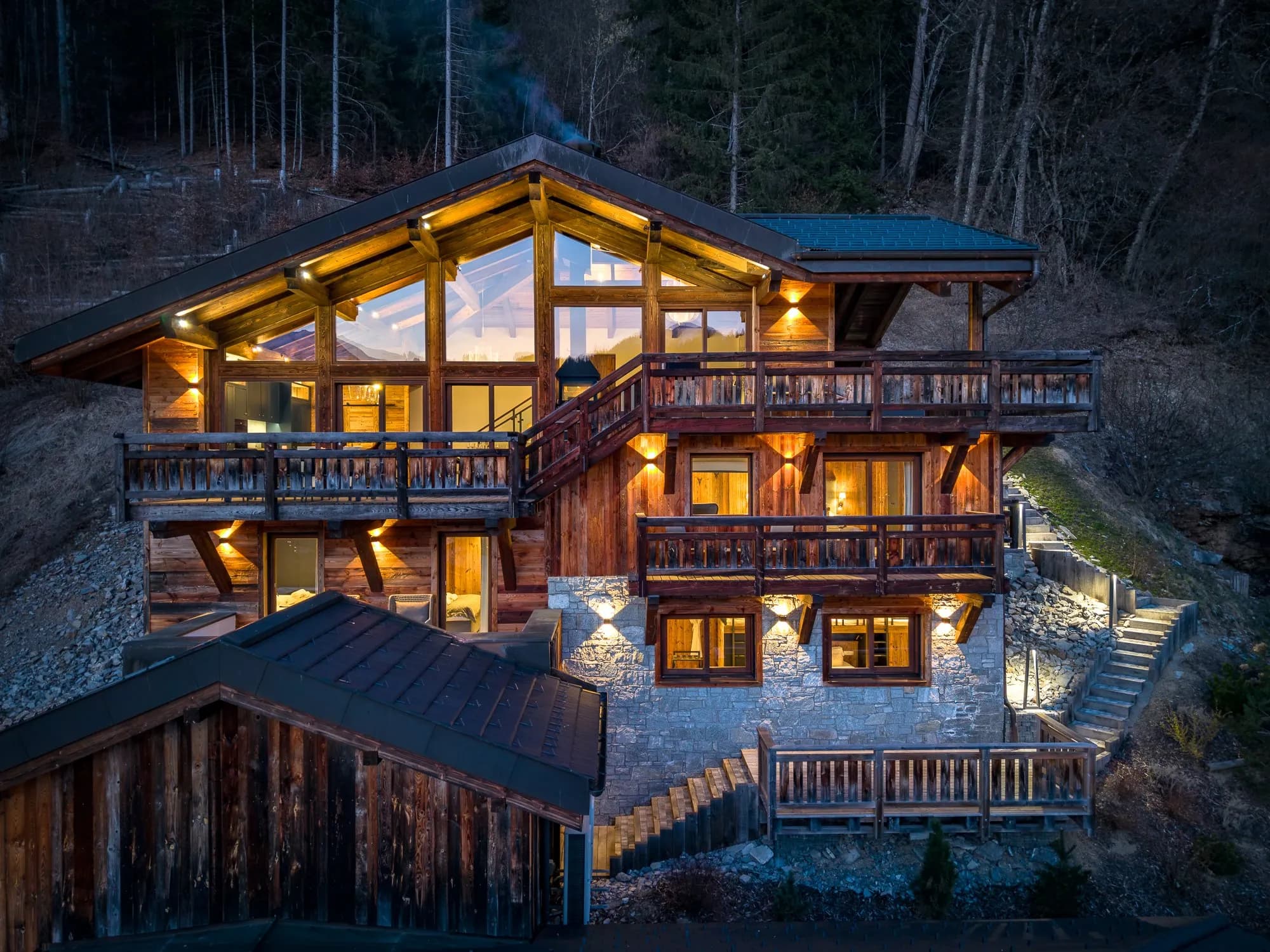 Multilevel mountain lodge with stacked decks, stone base, and ambient lighting throughout