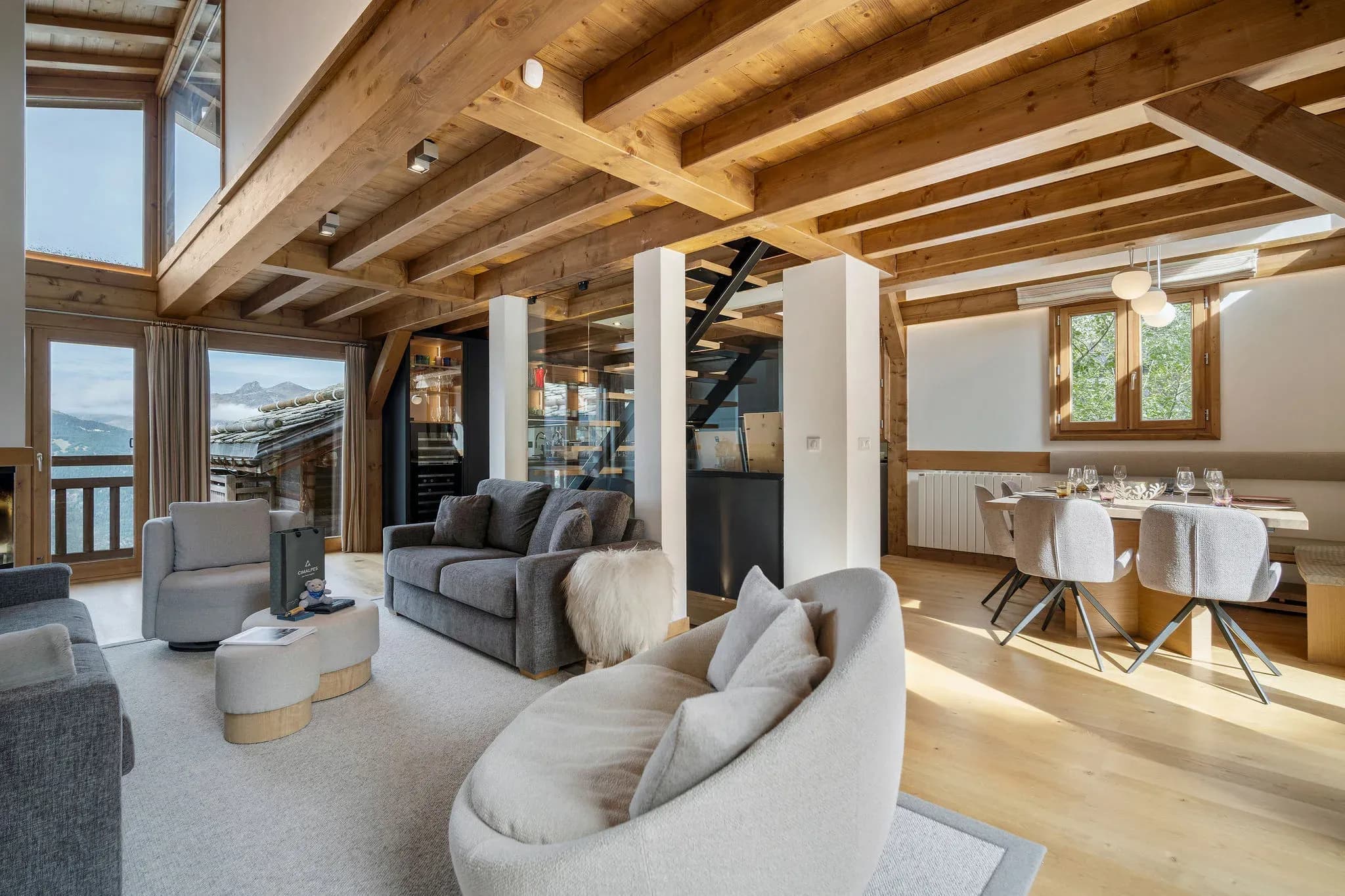 Lounge with grey sofas, round armchair and dining table beside mountain-view windows