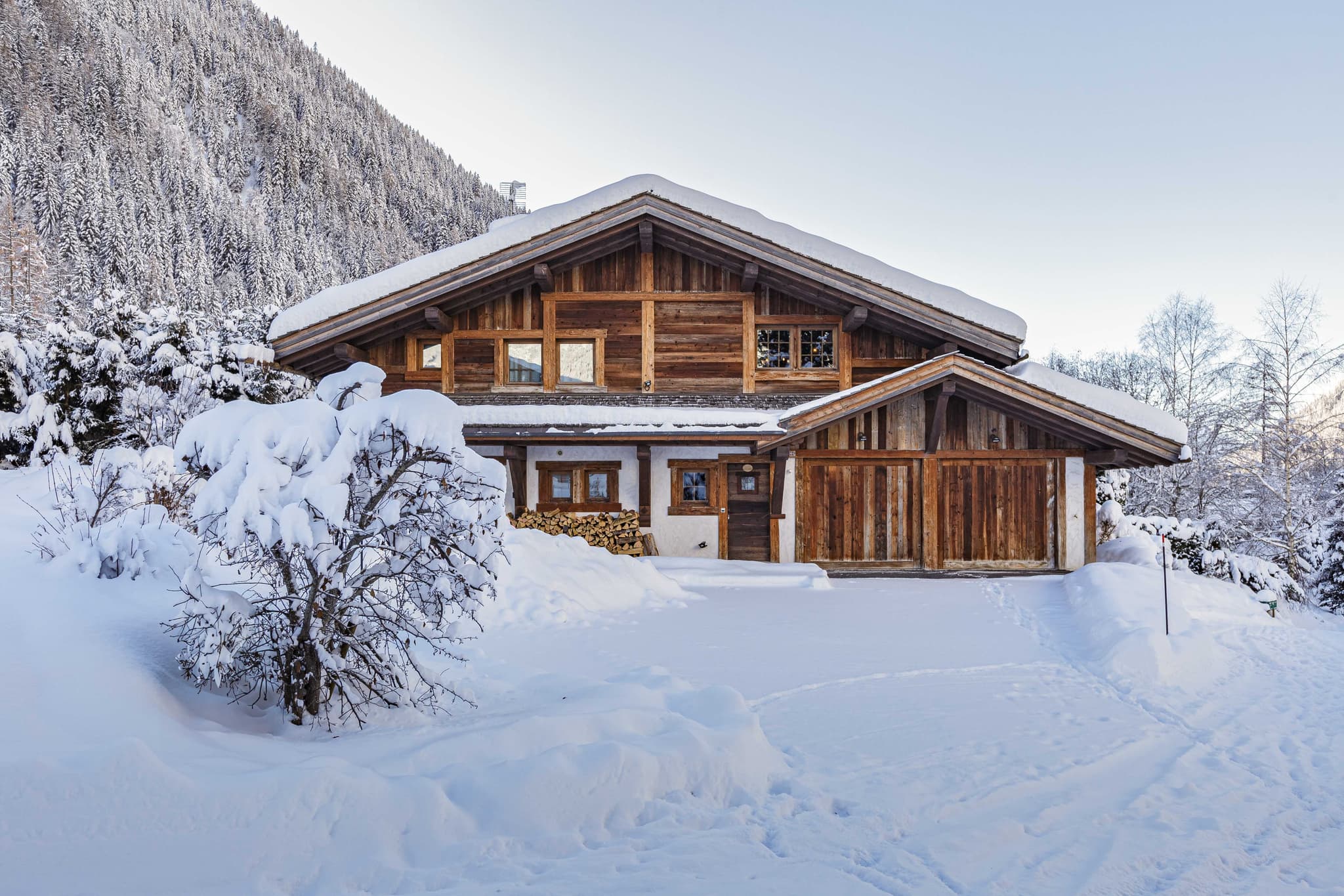 Snow-covered timber chalet beneath a forested mountain slope