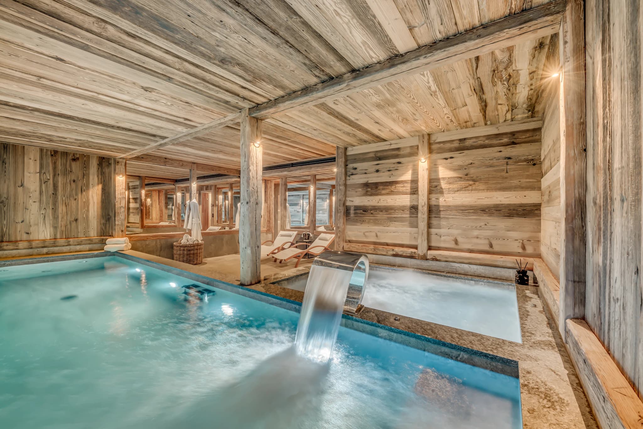 Indoor swimming pool with a water feature and poolside loungers