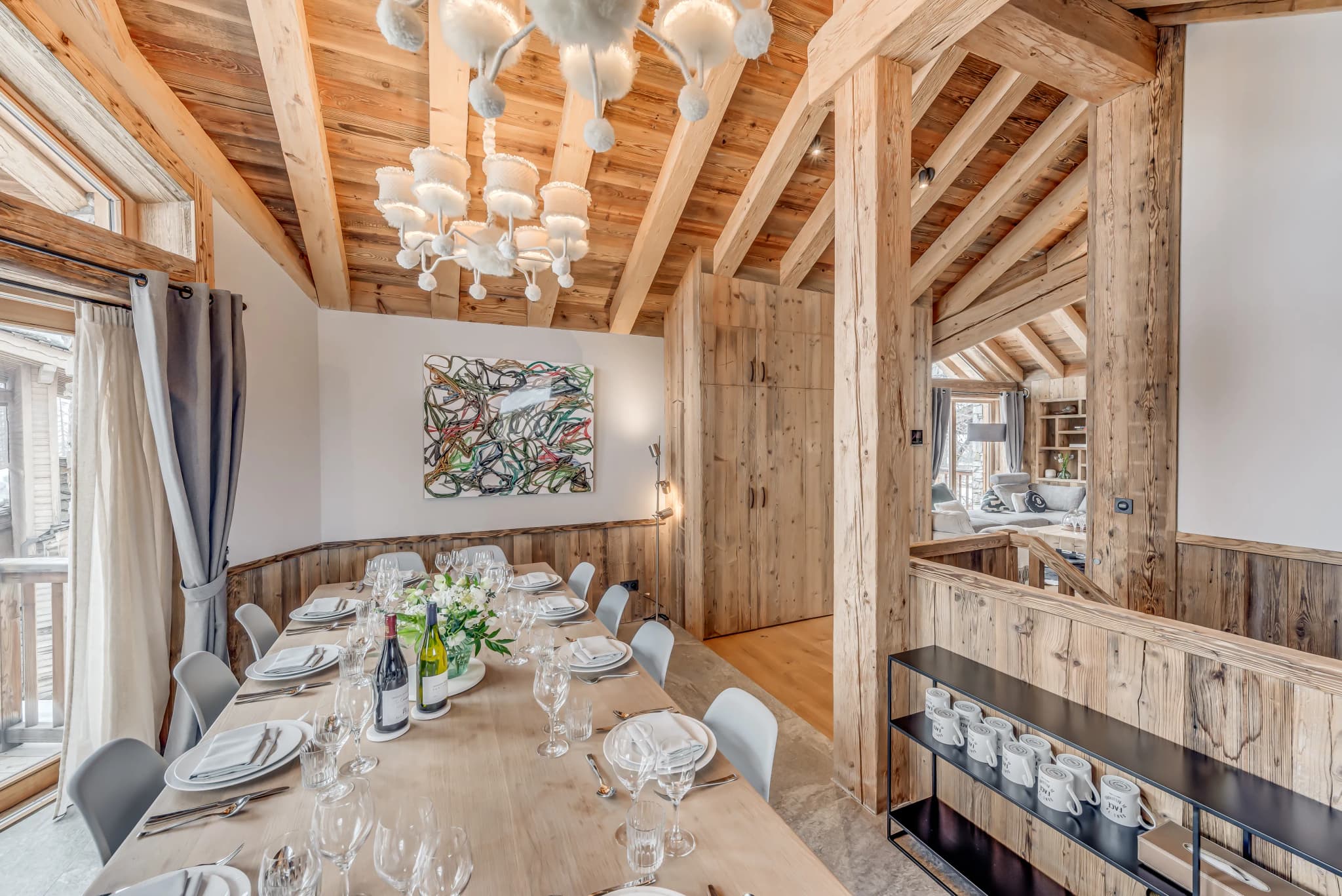 Dining table under chandelier lighting beside large windows