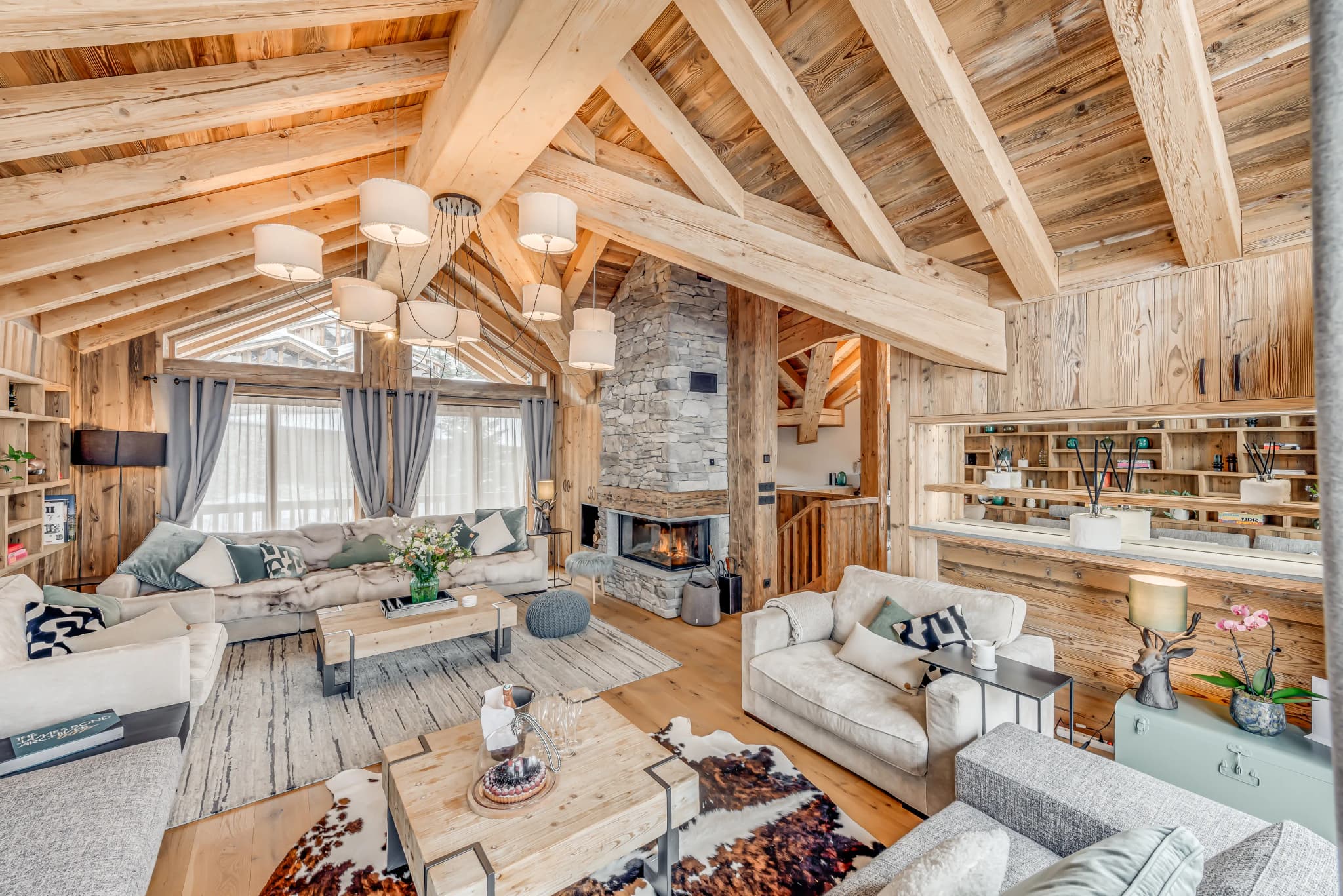 Living room beneath exposed beams with a central stone fireplace