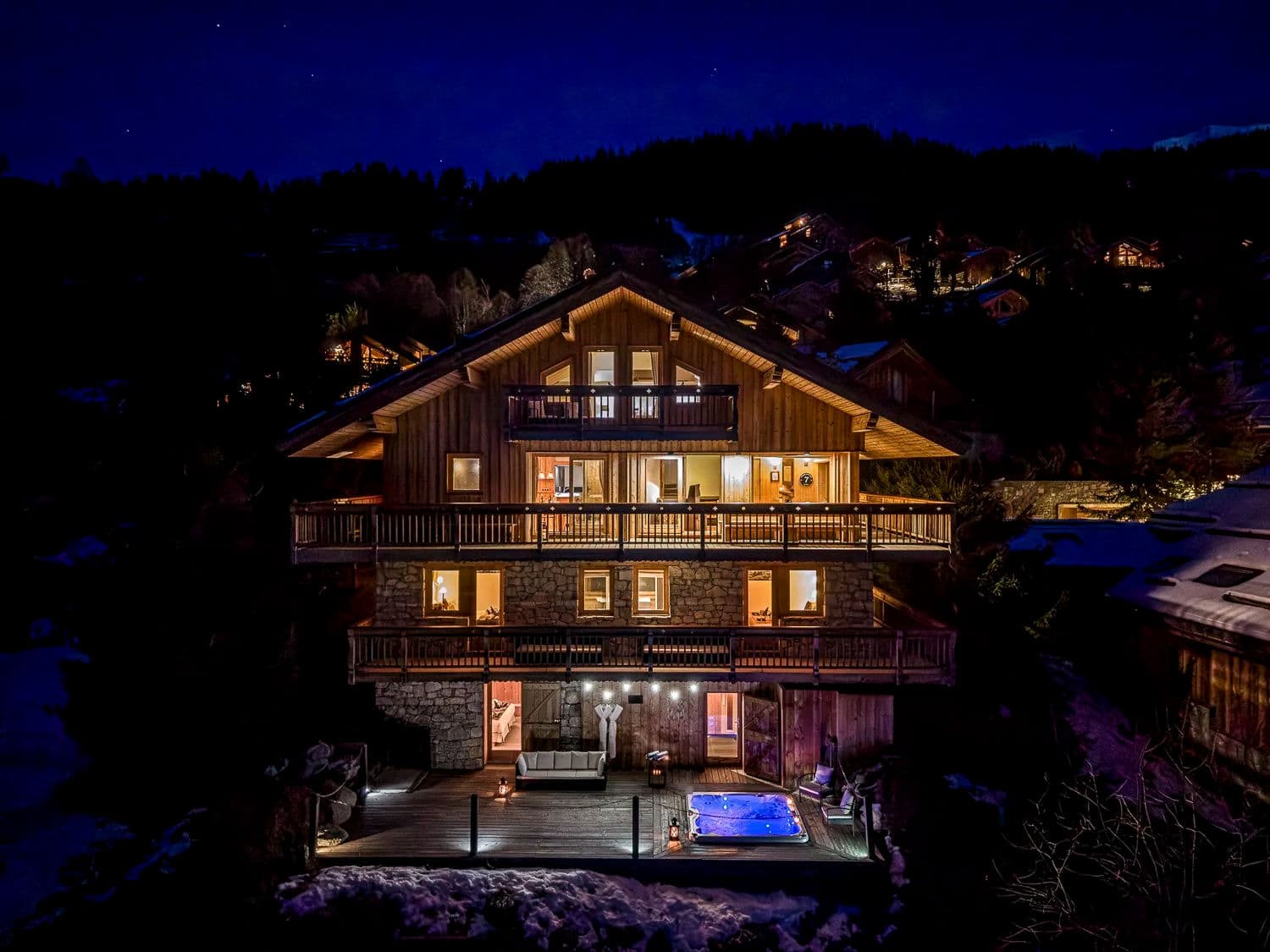 Hillside chalet lit at night; heated outdoor hot tub on lower deck