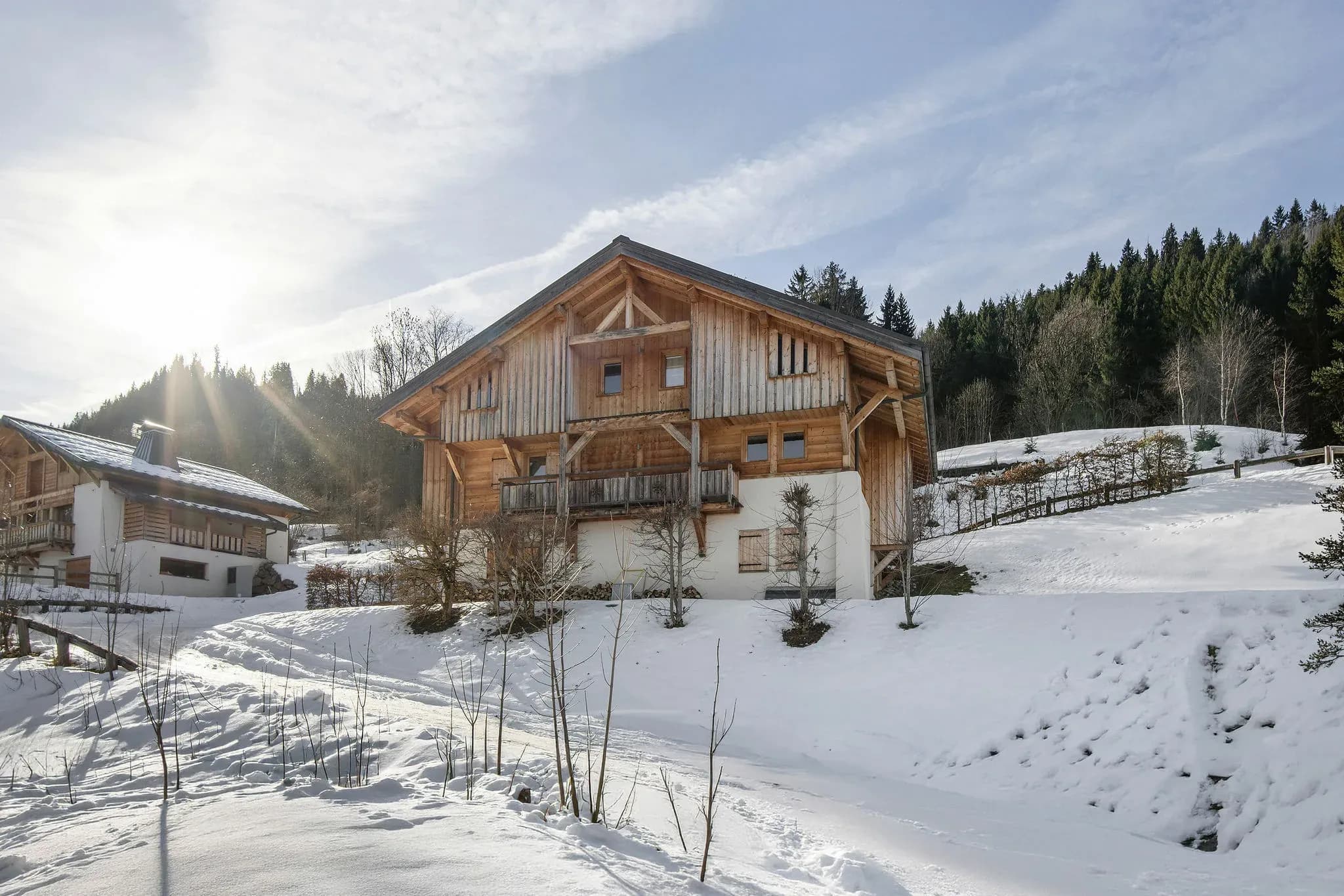 Timber chalet on a snowy slope with balcony and wooded hillside behind