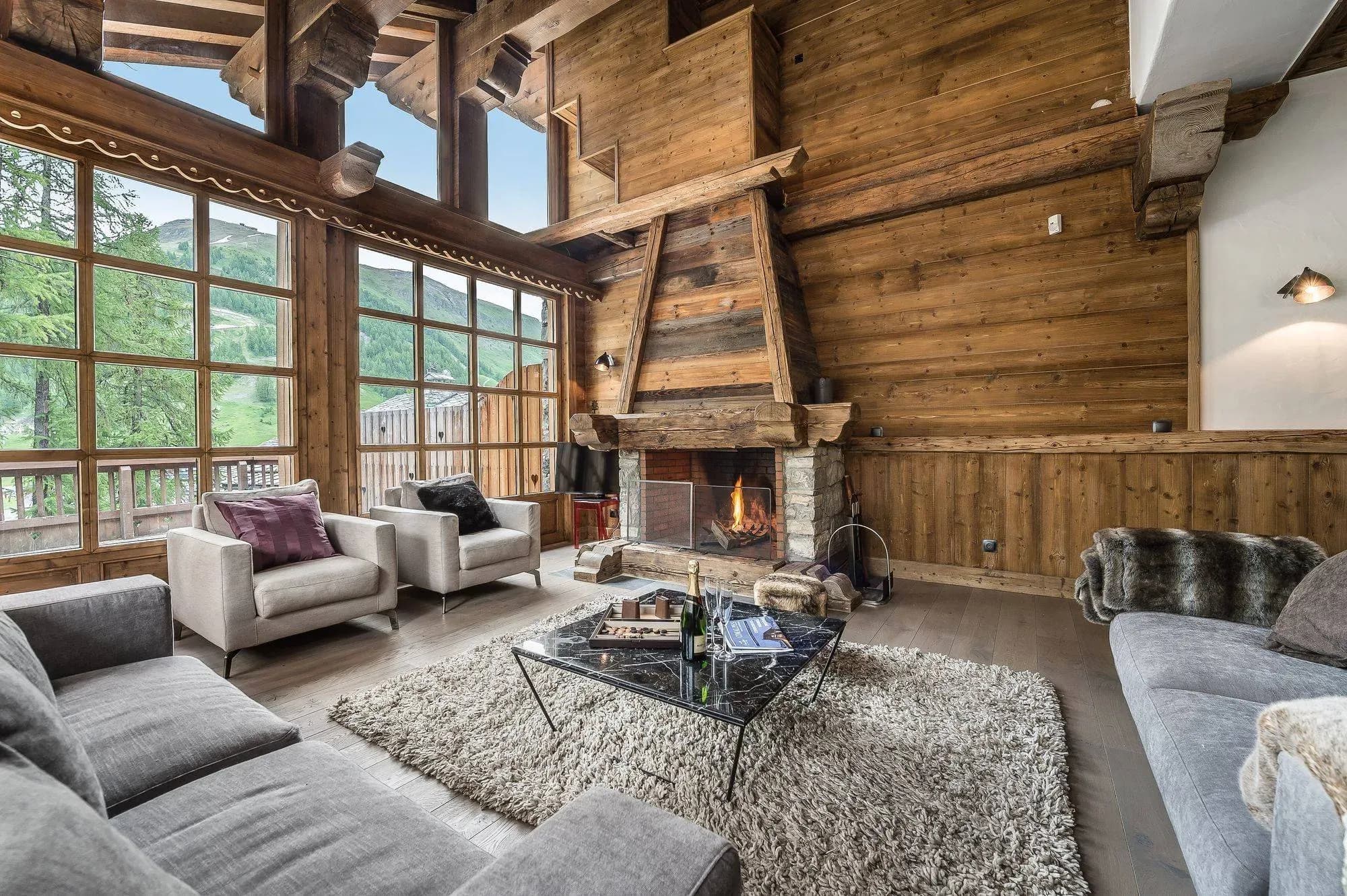 Living room with stone fireplace, two sofas, armchairs and floor-to-ceiling mountain-view windows