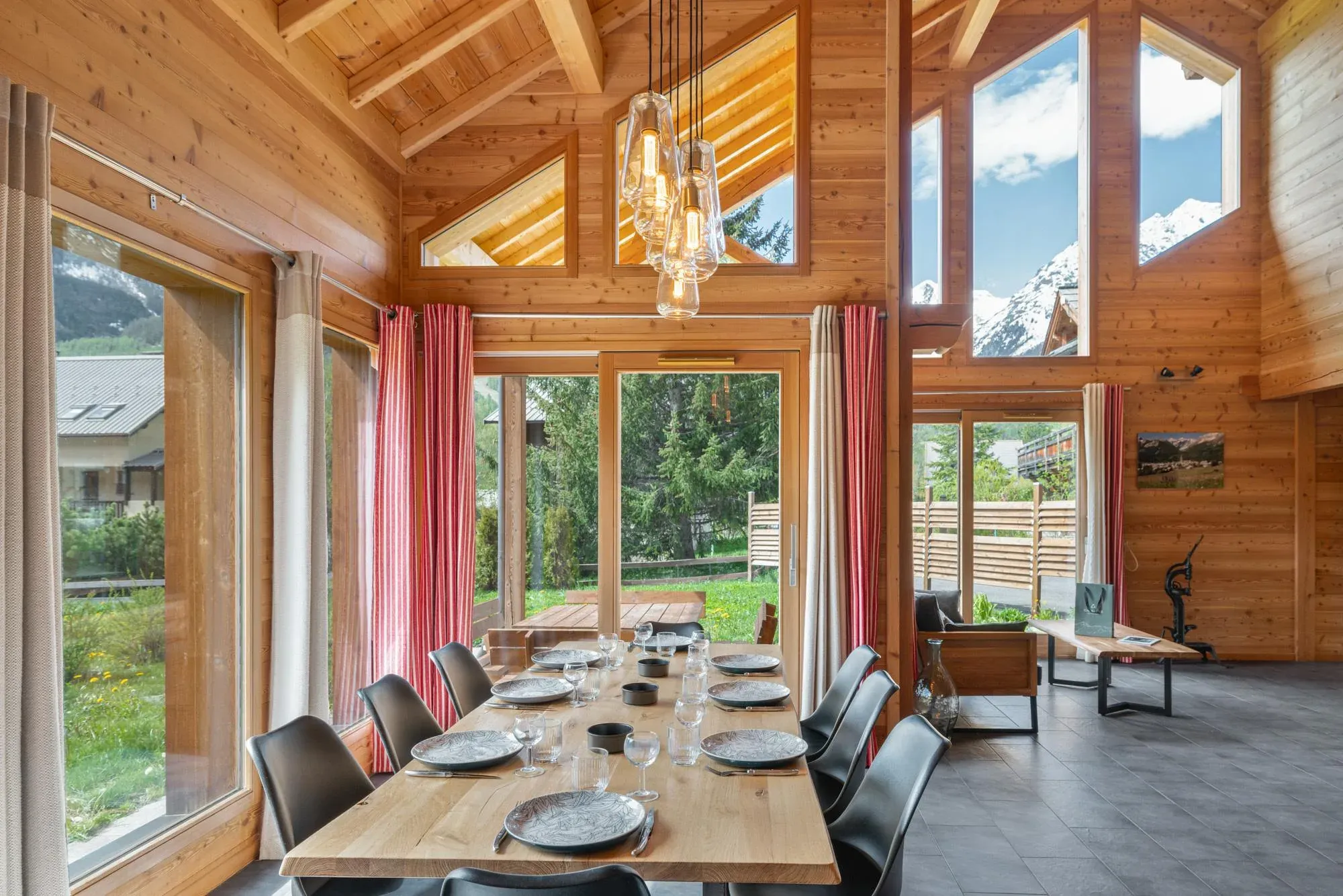Dining area with wooden table set for eight, floor-to-ceiling windows and mountain view