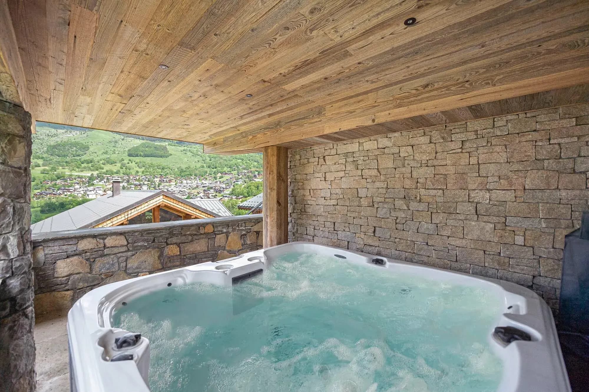 Covered outdoor hot tub with stone walls and village view