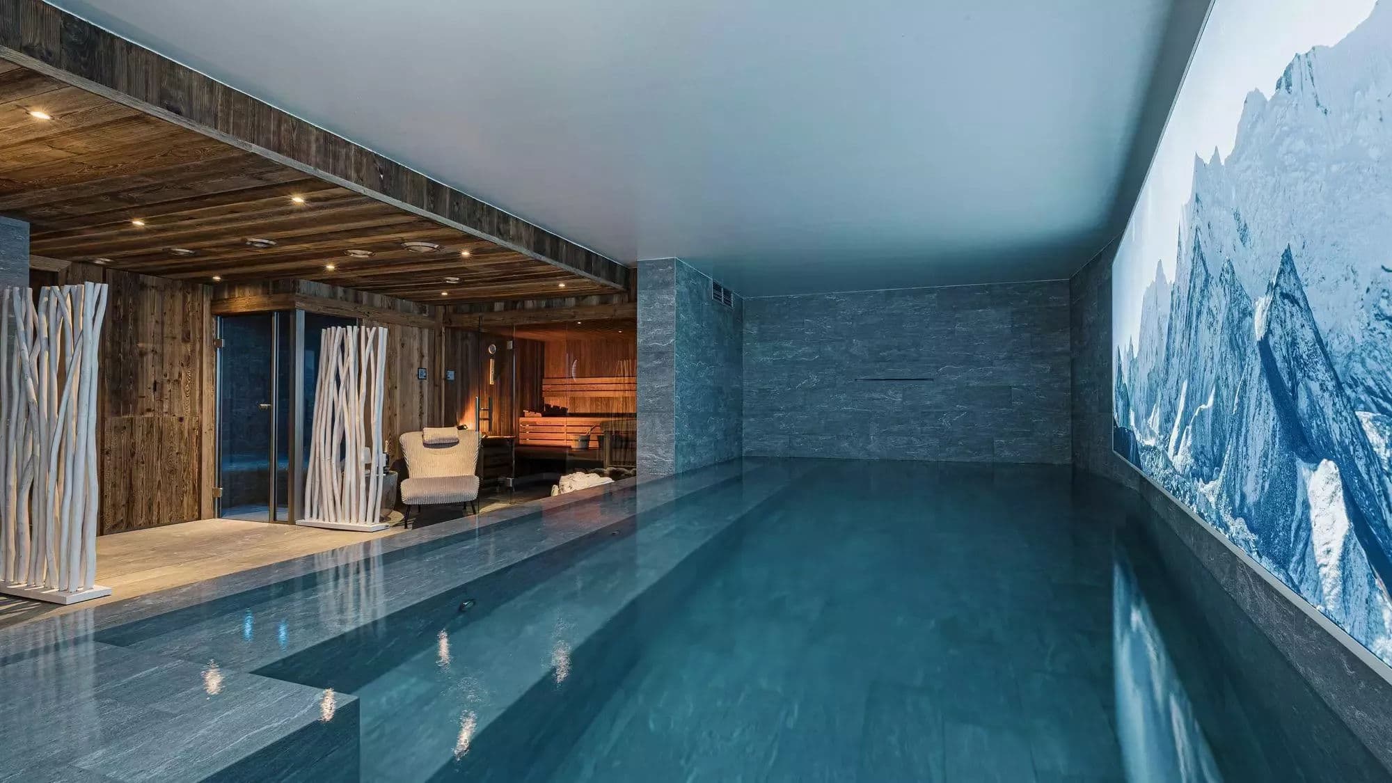 Indoor swimming pool with illuminated mountain wall and adjacent relaxation area