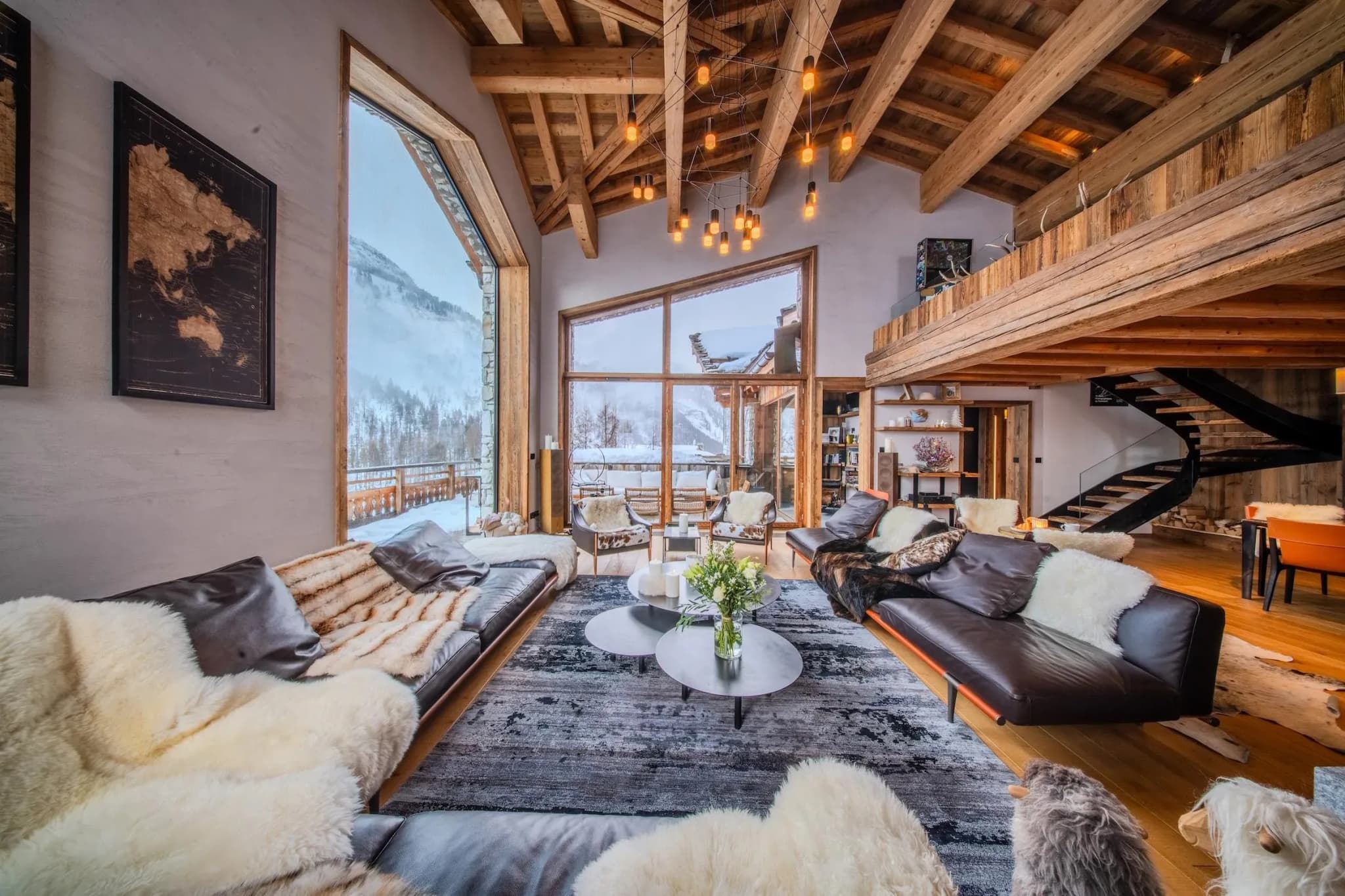 Living room with leather sofas, sheepskin throws and floor-to-ceiling window onto snowy mountains