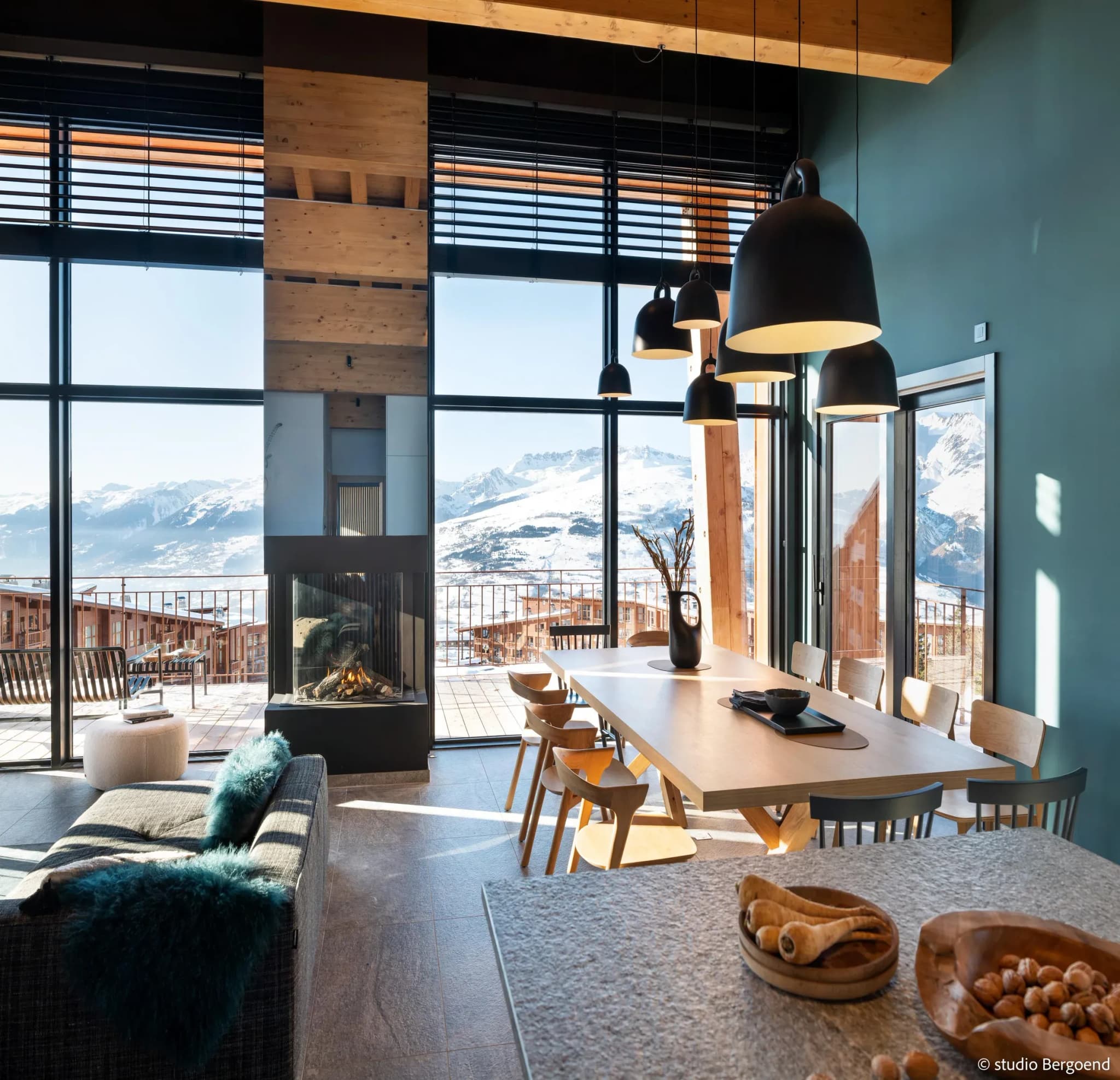Dining area with wooden table, black pendant lights and mountain views through floor-to-ceiling windows