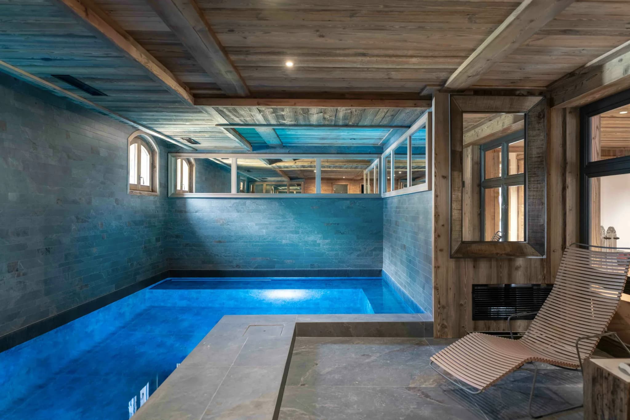 Indoor pool with slate walls and wooden ceiling beams, loungers beside it