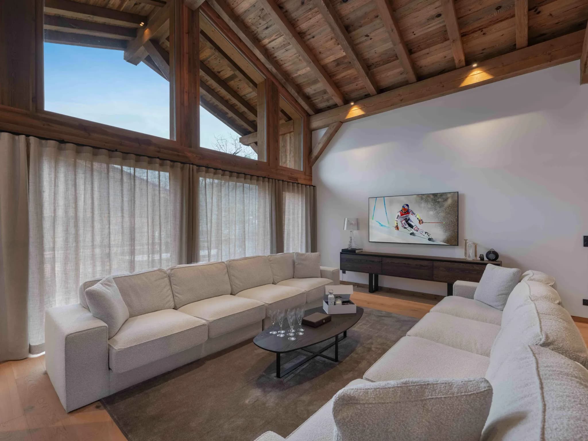 Living room with L-shaped sofa, TV and tall windows with linen curtains