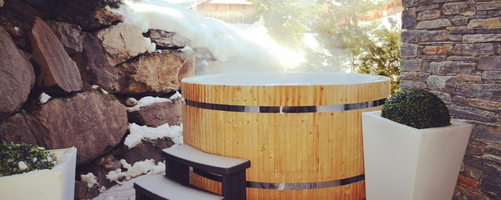 Outdoor cedar hot tub surrounded by snow-covered stonework