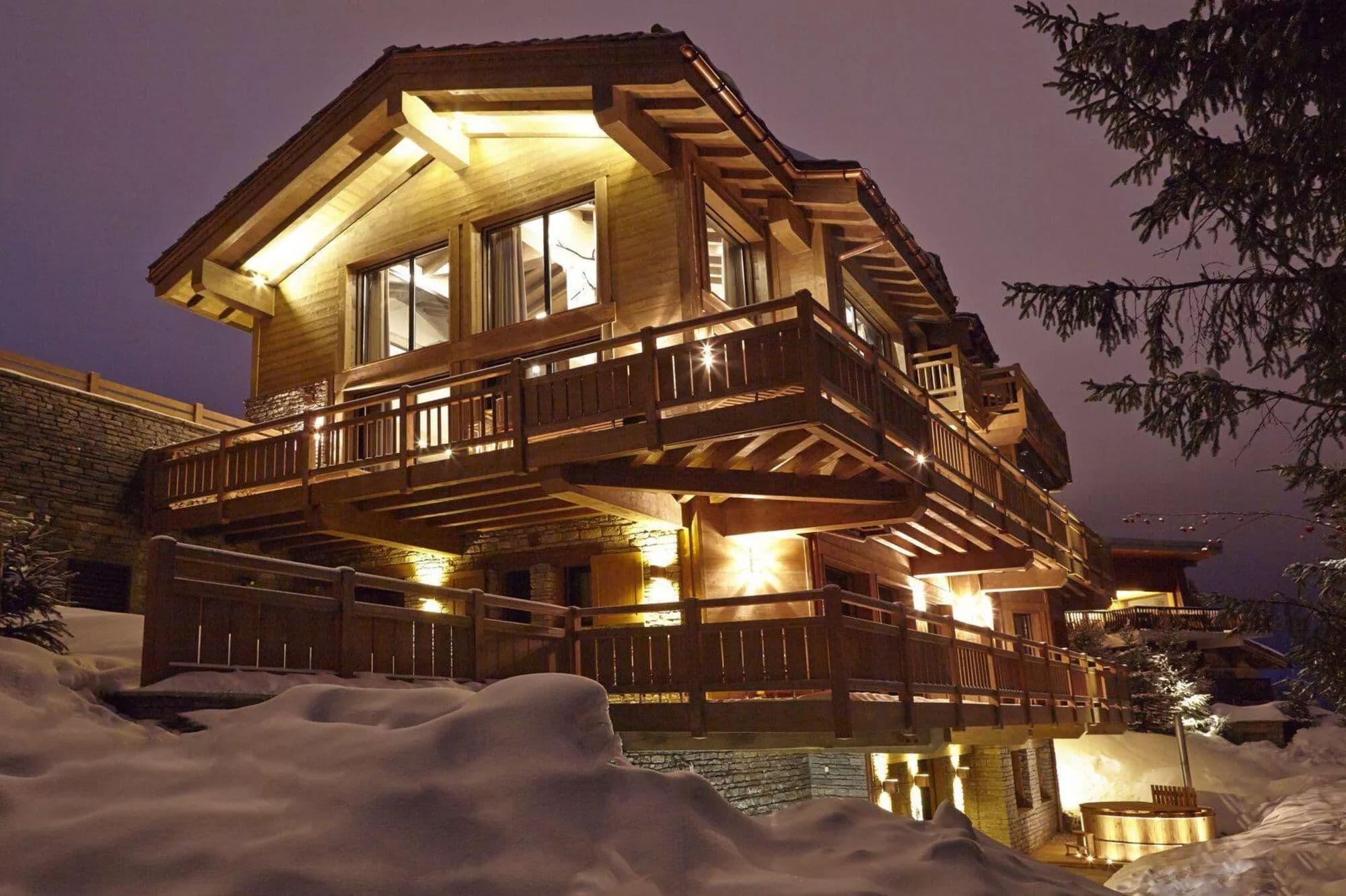 Chalet exterior at dusk with snow-covered terraces and balconies