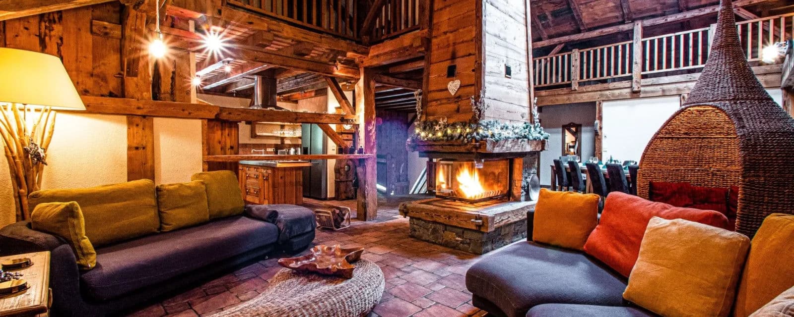 Open-plan living room with a central open fireplace, sofas and exposed timber beams