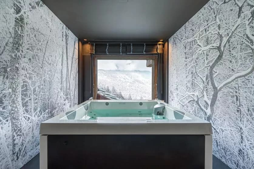 Indoor jacuzzi beside a window and a forest mural