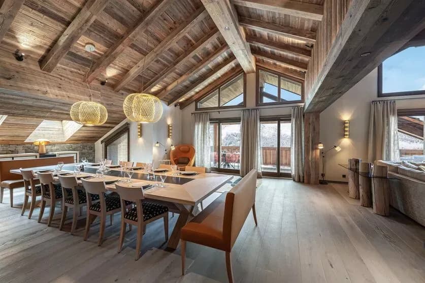 Dining area beneath a vaulted timber ceiling with windows across the room