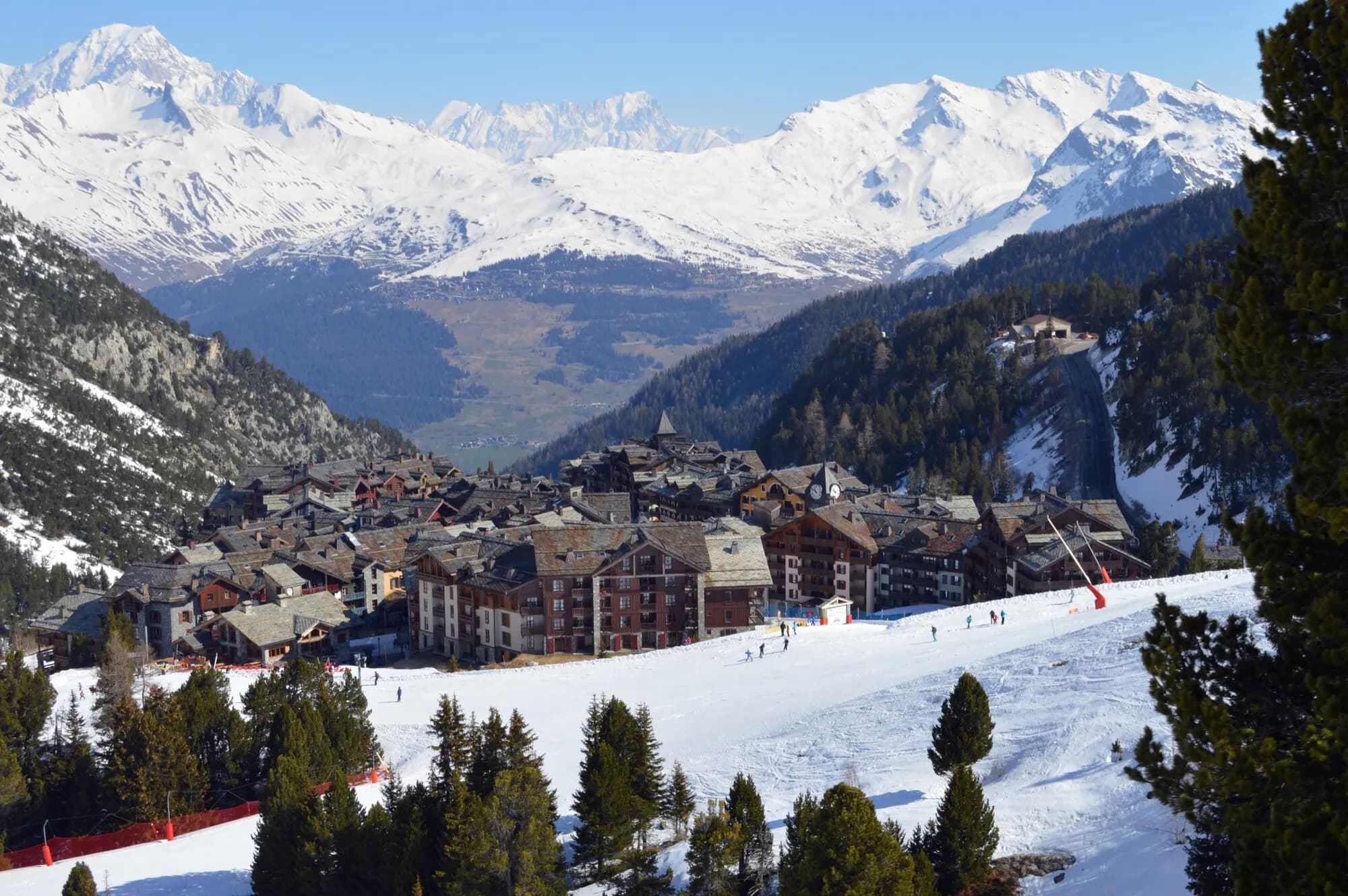 The chalet-style village of Arc 1950 among snowy pines, with the Mont Blanc range on the horizon.