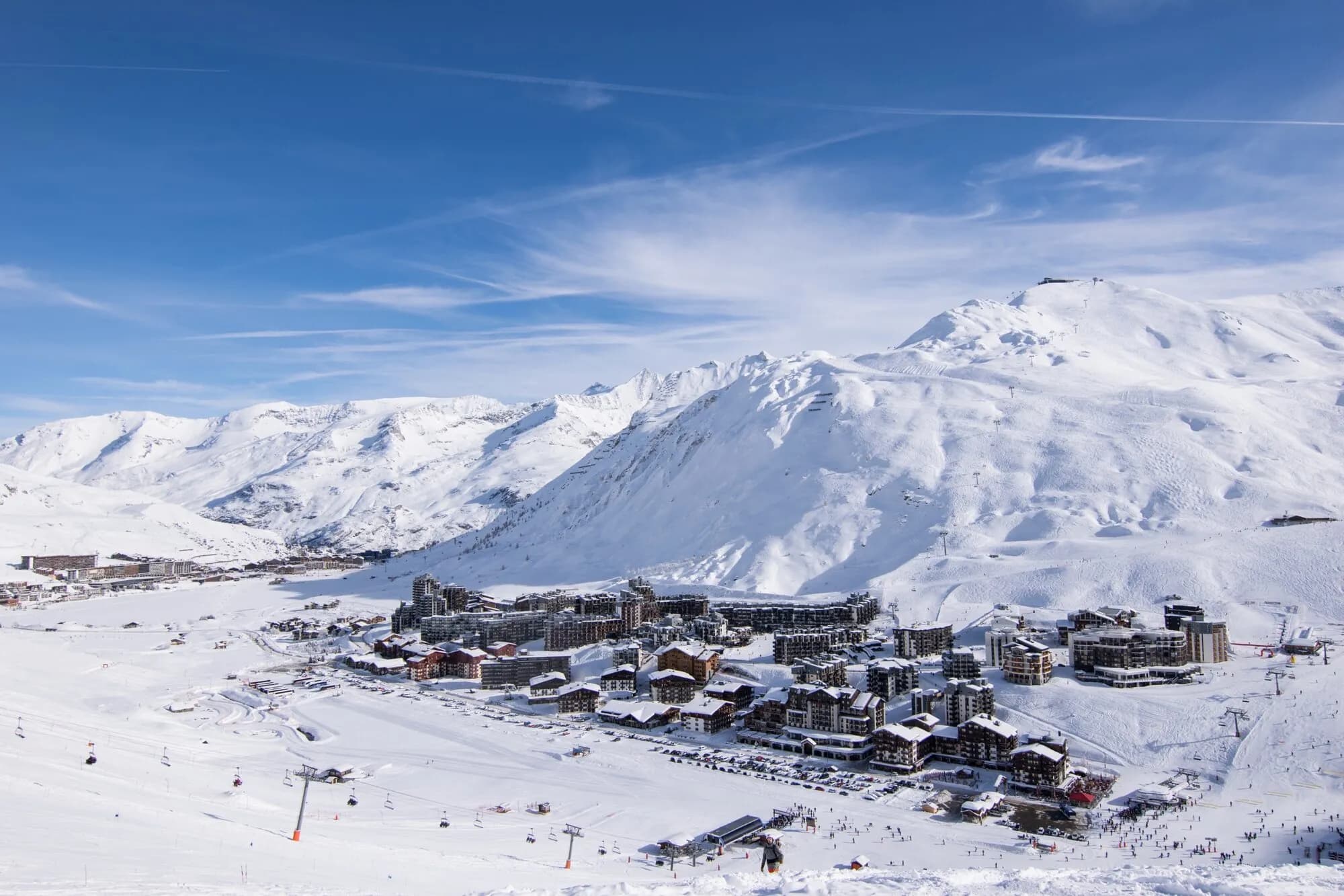 The resort buildings of Val Claret and Tignes le Lac sit in a snowy valley below rounded white mountains.