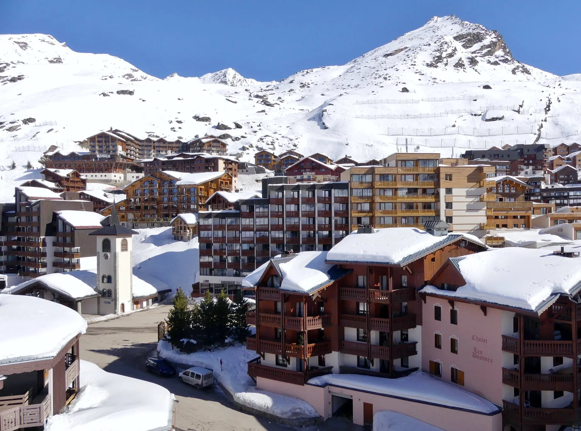 Snow-topped apartment buildings and the chapel of Val Thorens below a white mountain ridge.