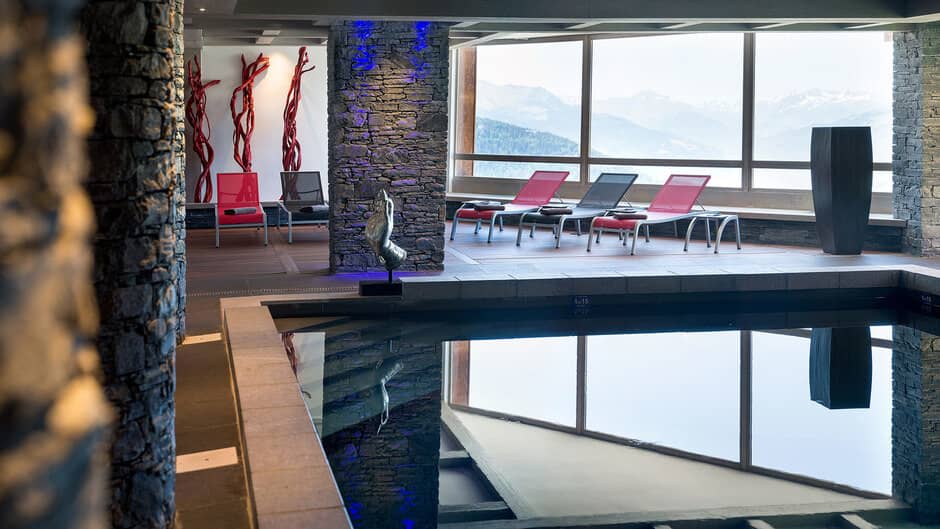 Indoor pool with stone pillars, sun loungers, and mountain views