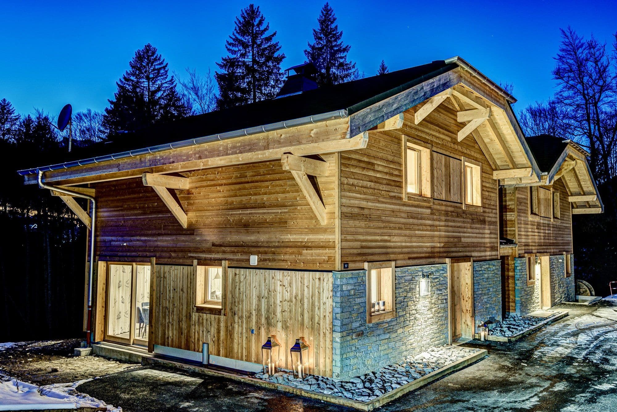 Elevated home with stone foundation, timber siding, and covered outdoor deck with lighting