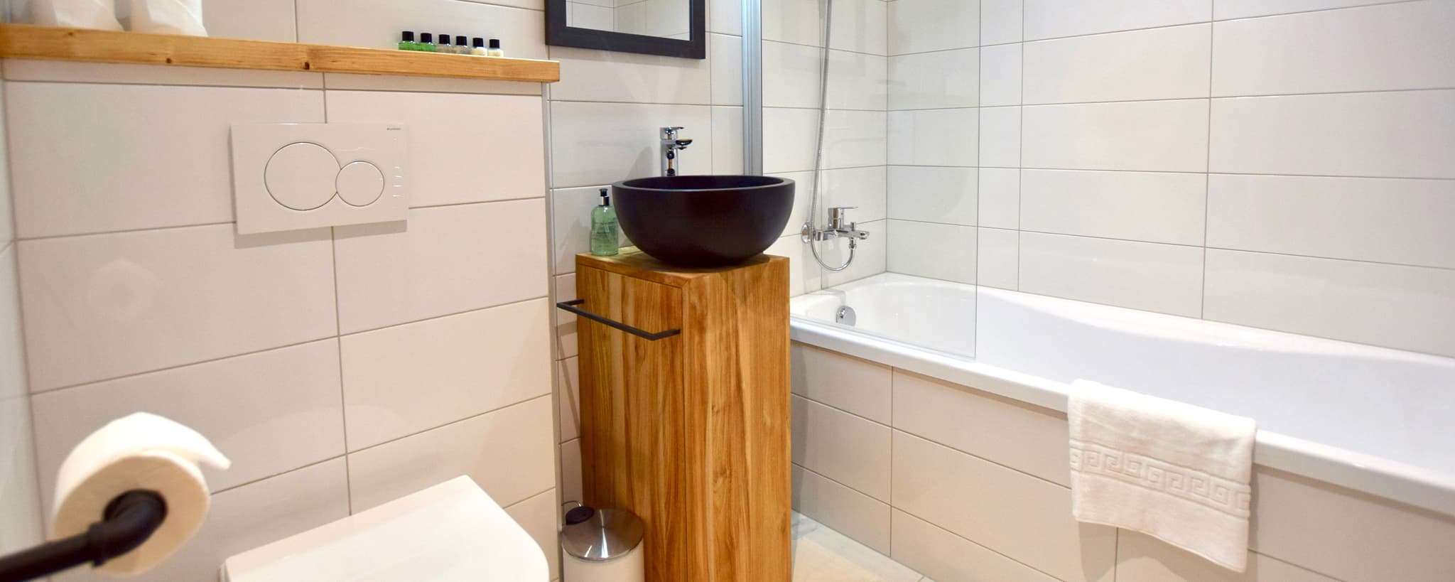 Bathroom with black vessel sink, wooden vanity, and separate soaking tub