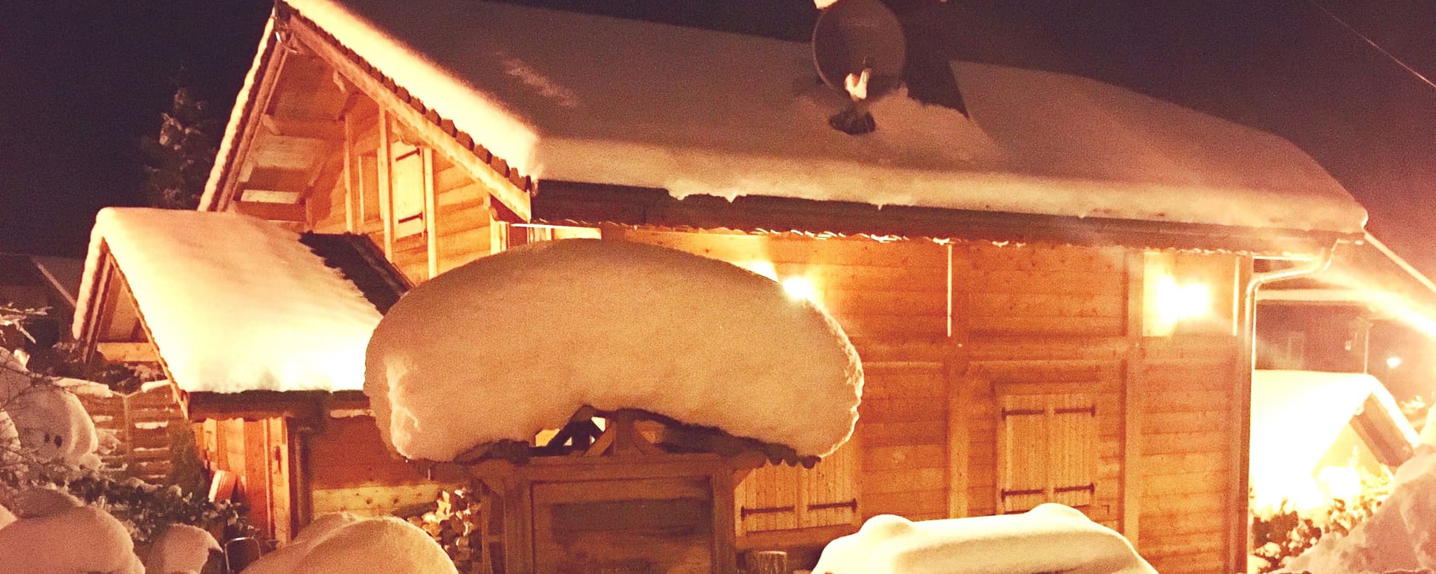 Snow-covered log cabin exterior with warm uplighting and decorated eaves