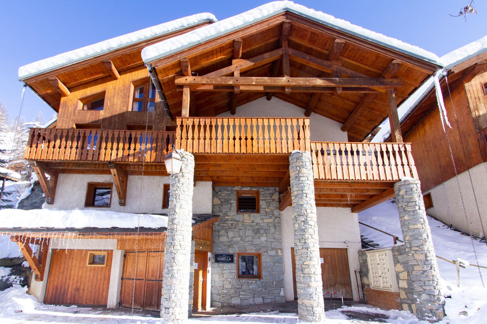 Alpine chalet exterior with stone pillars, wood balconies, and snow-covered pitched roof