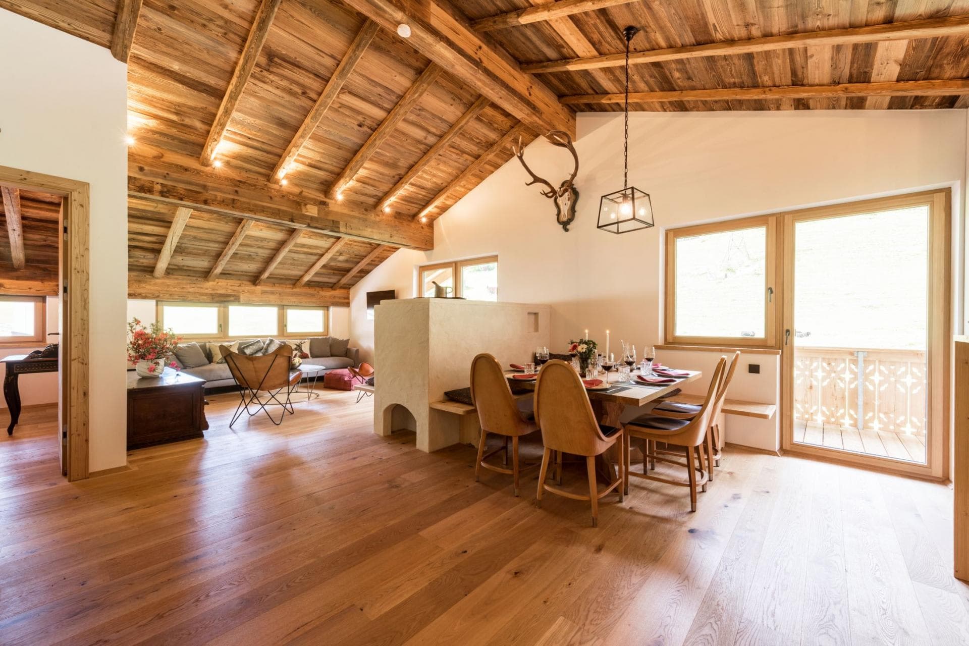 Open-plan dining and living area with vaulted timber ceilings and balcony access