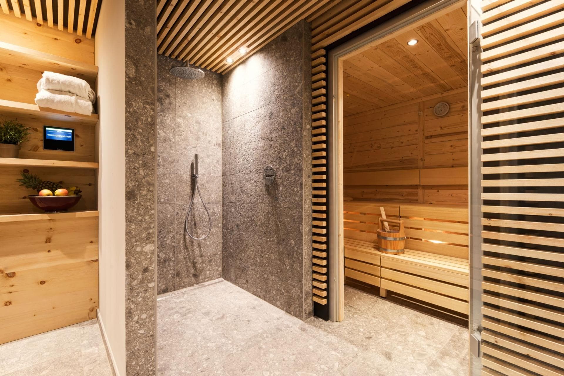 Stone walk-in rainfall shower adjacent to private wood-paneled sauna