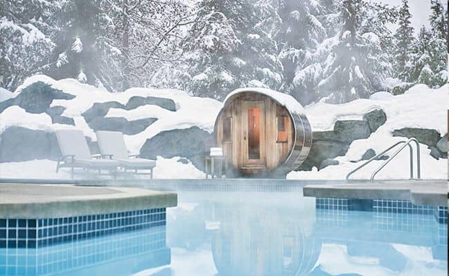 Outdoor barrel sauna and heated pool with snowy forest backdrop