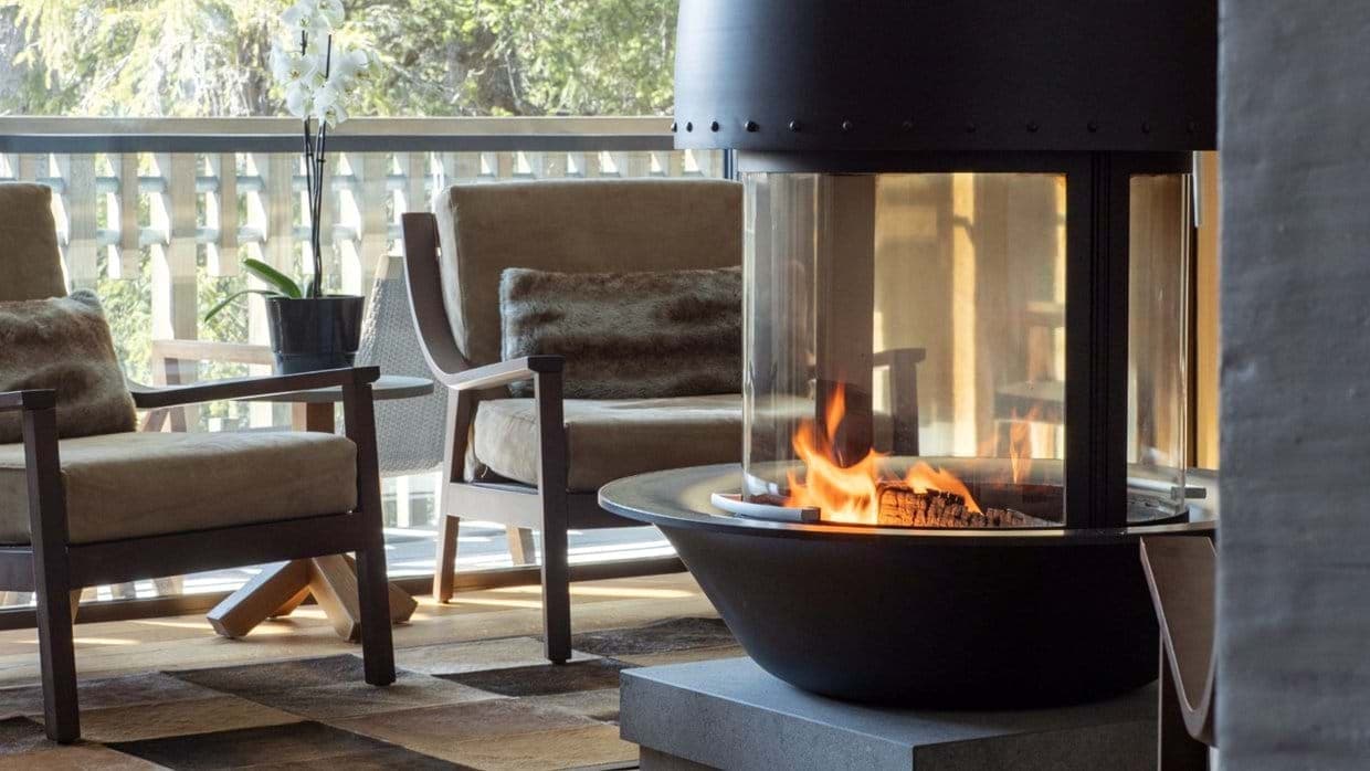 Lounge seating with 360-degree glass fireplace and forest view