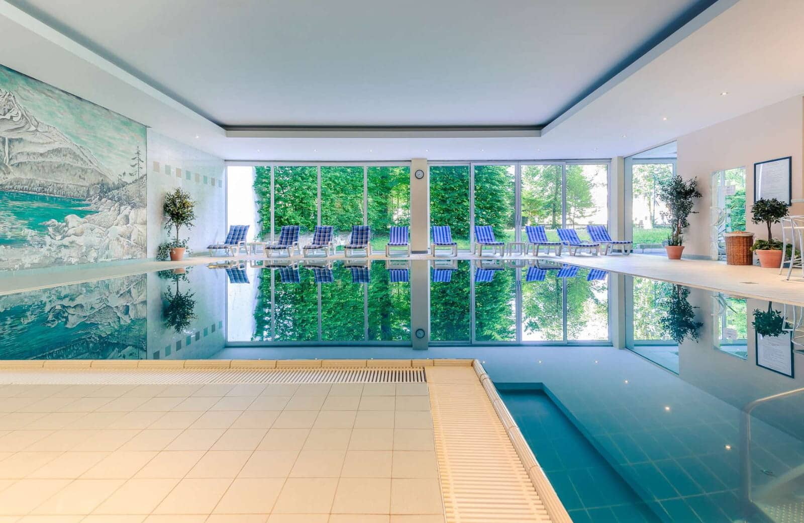 Indoor pool with floor-to-ceiling garden views and lounge seating