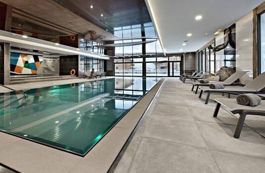 Indoor heated pool with poolside loungers and floor-to-ceiling windows